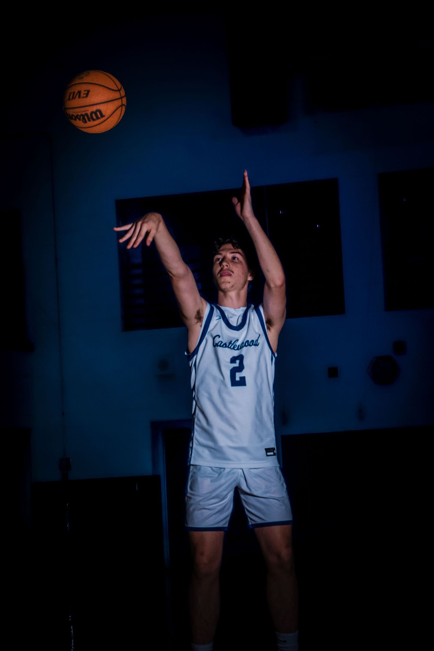 Player in Castlewood uniform practices shooting form in blue-lit gymnasium.