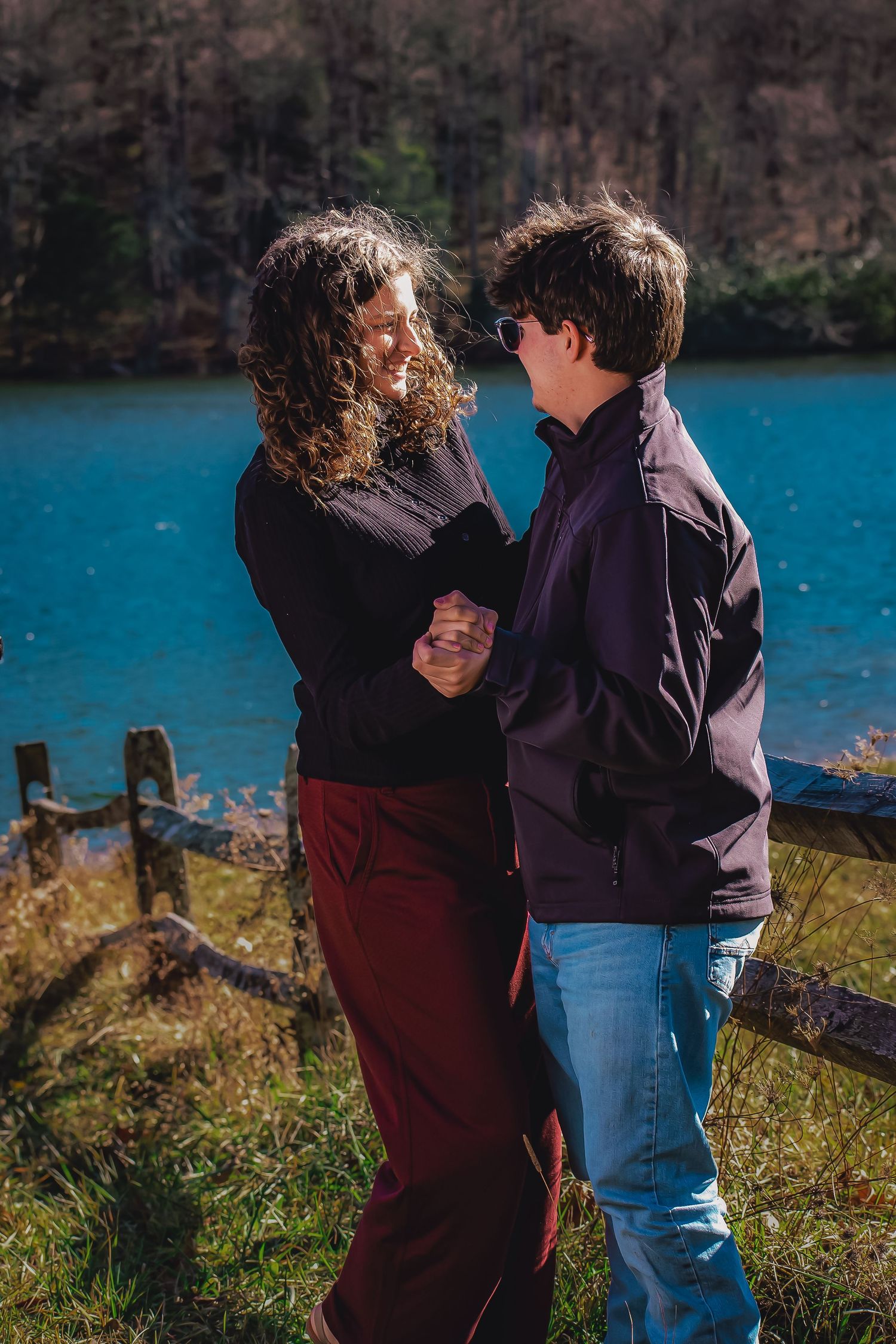 Two people sharing an intimate dance moment near a blue lake with rustic fencing.