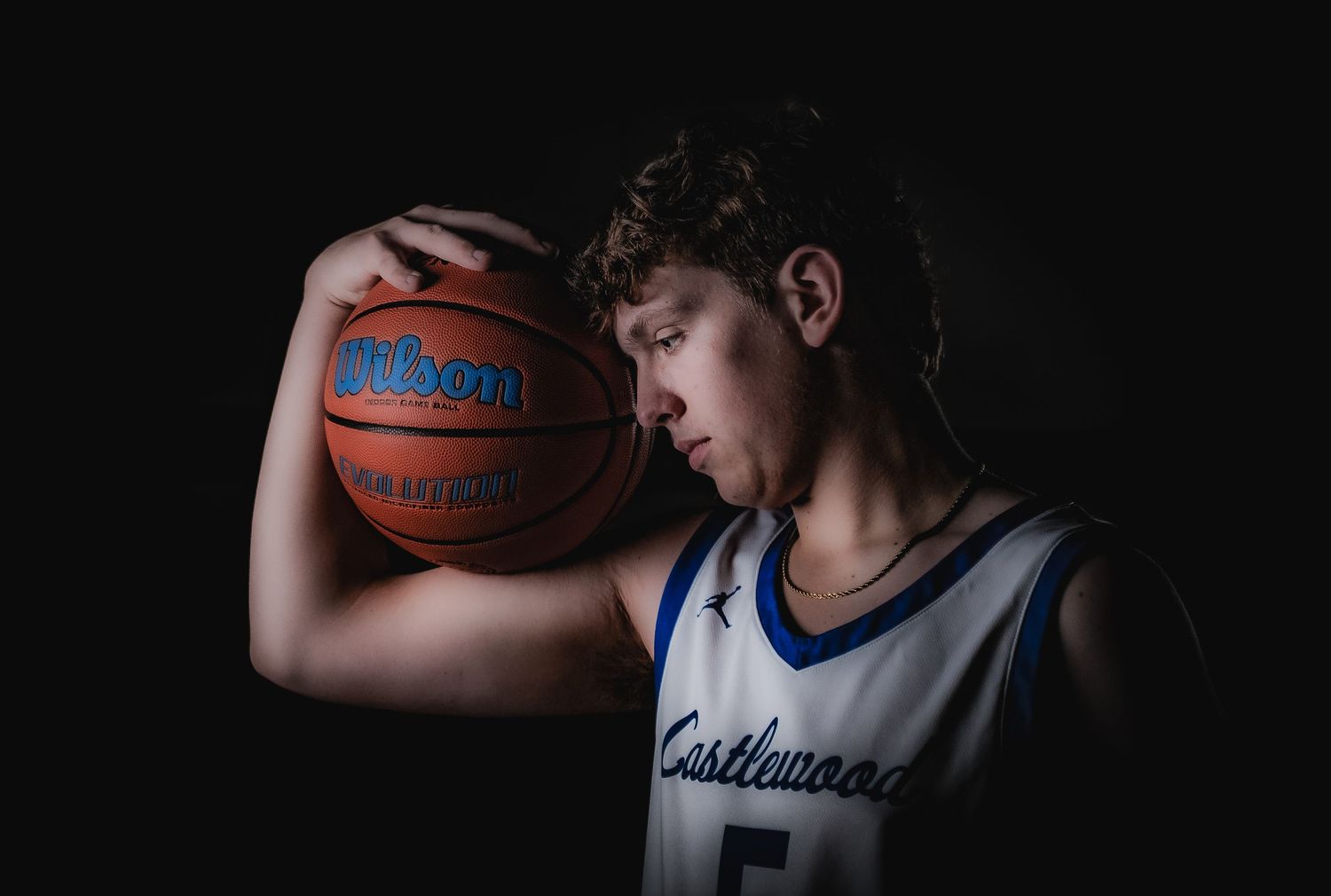Basketball player dribbles in white uniform with dramatic shadows and lighting effects.