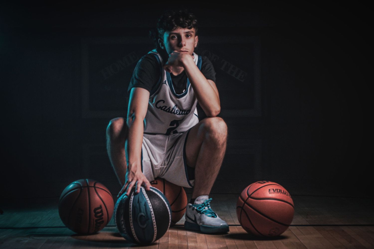 Player poses with multiple basketballs on dark wooden floor with dramatic lighting.