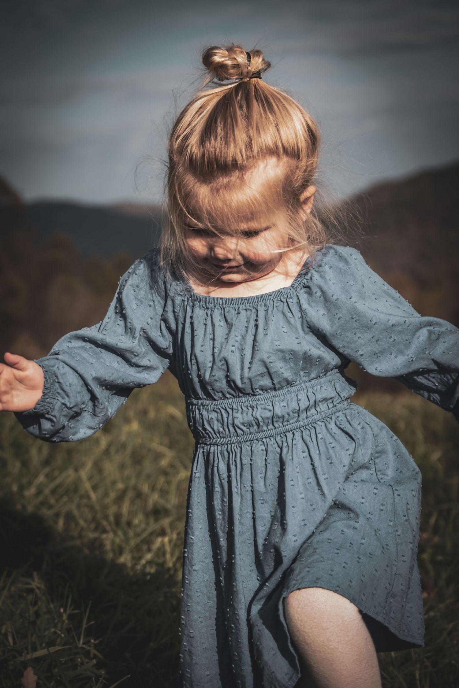 Child twirling in blue dress on hillside during golden hour.