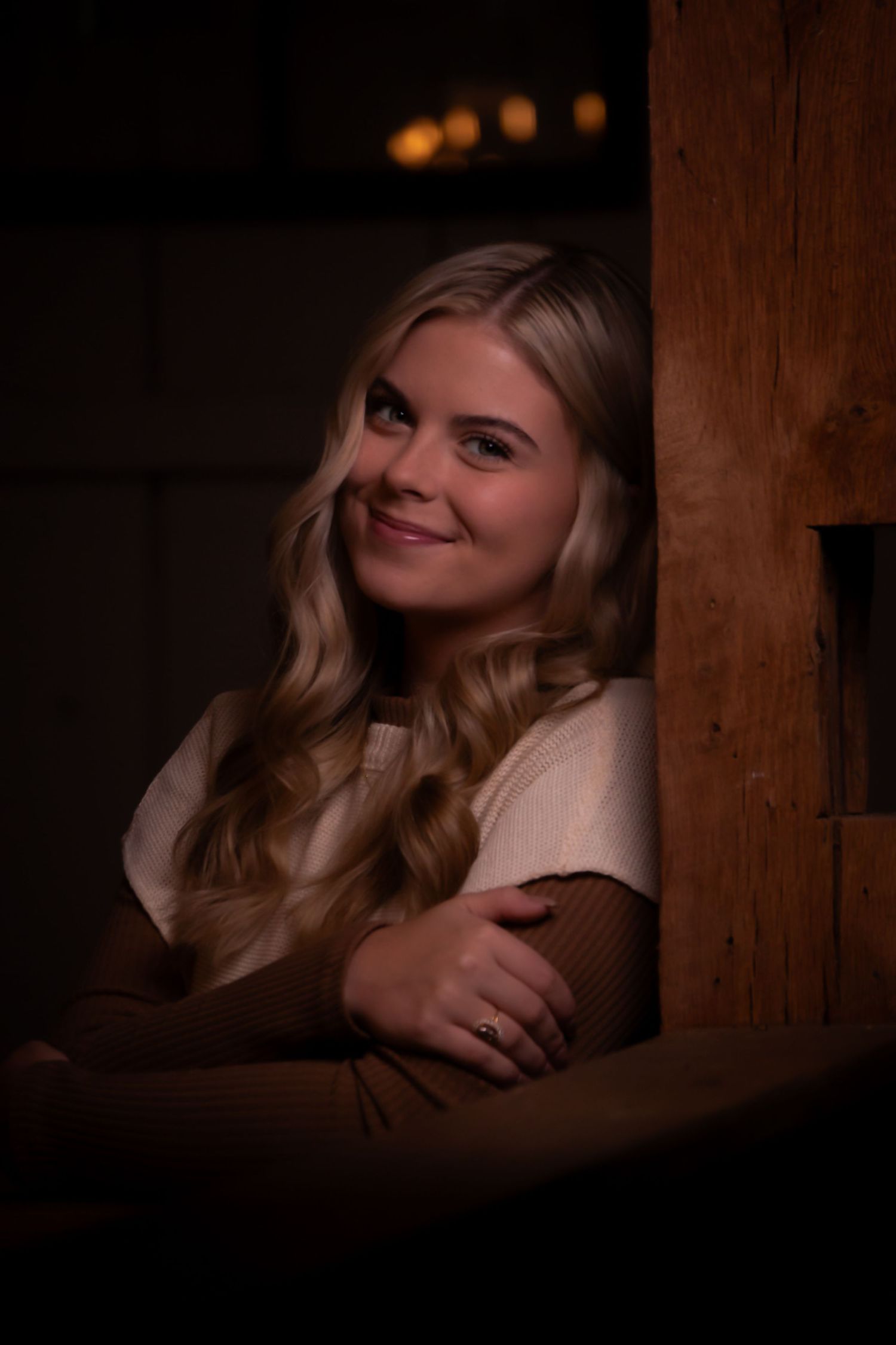 Warm indoor portrait with cream and brown top against wooden backdrop with soft lighting.