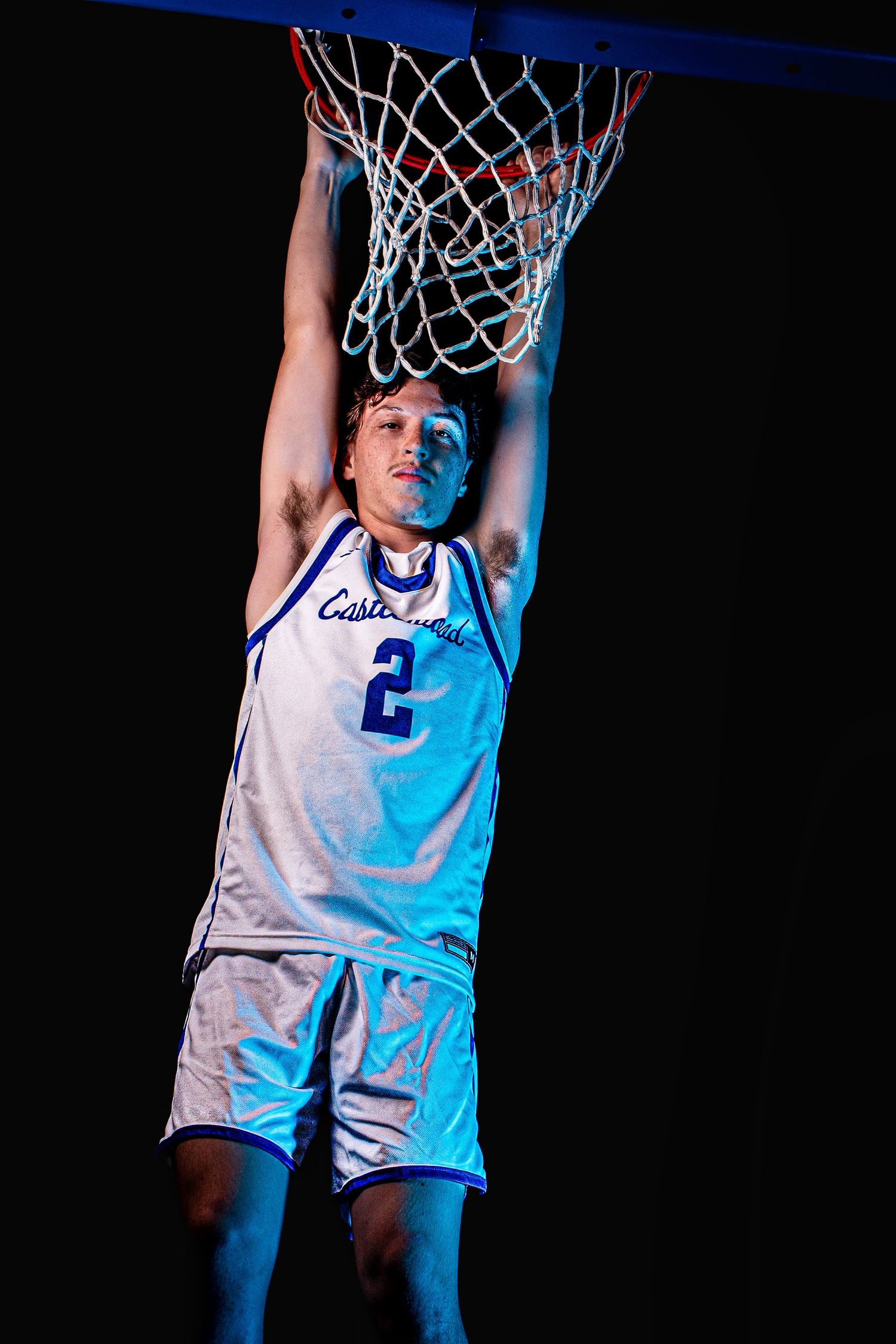 Basketball player in white jersey number 2 reaches up toward hoop with blue lighting.