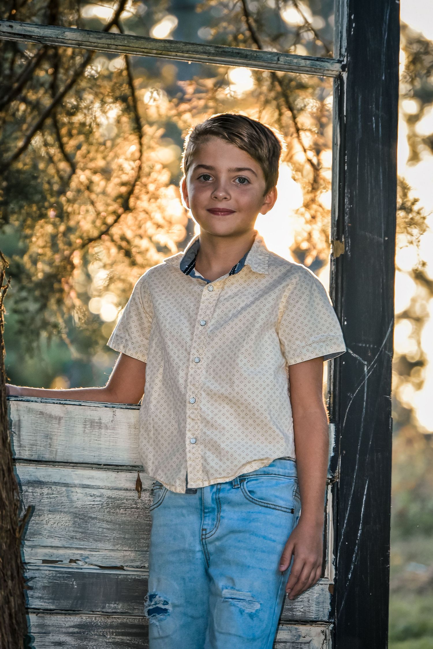 Child in casual attire posing against rustic wooden backdrop during golden hour photo session.