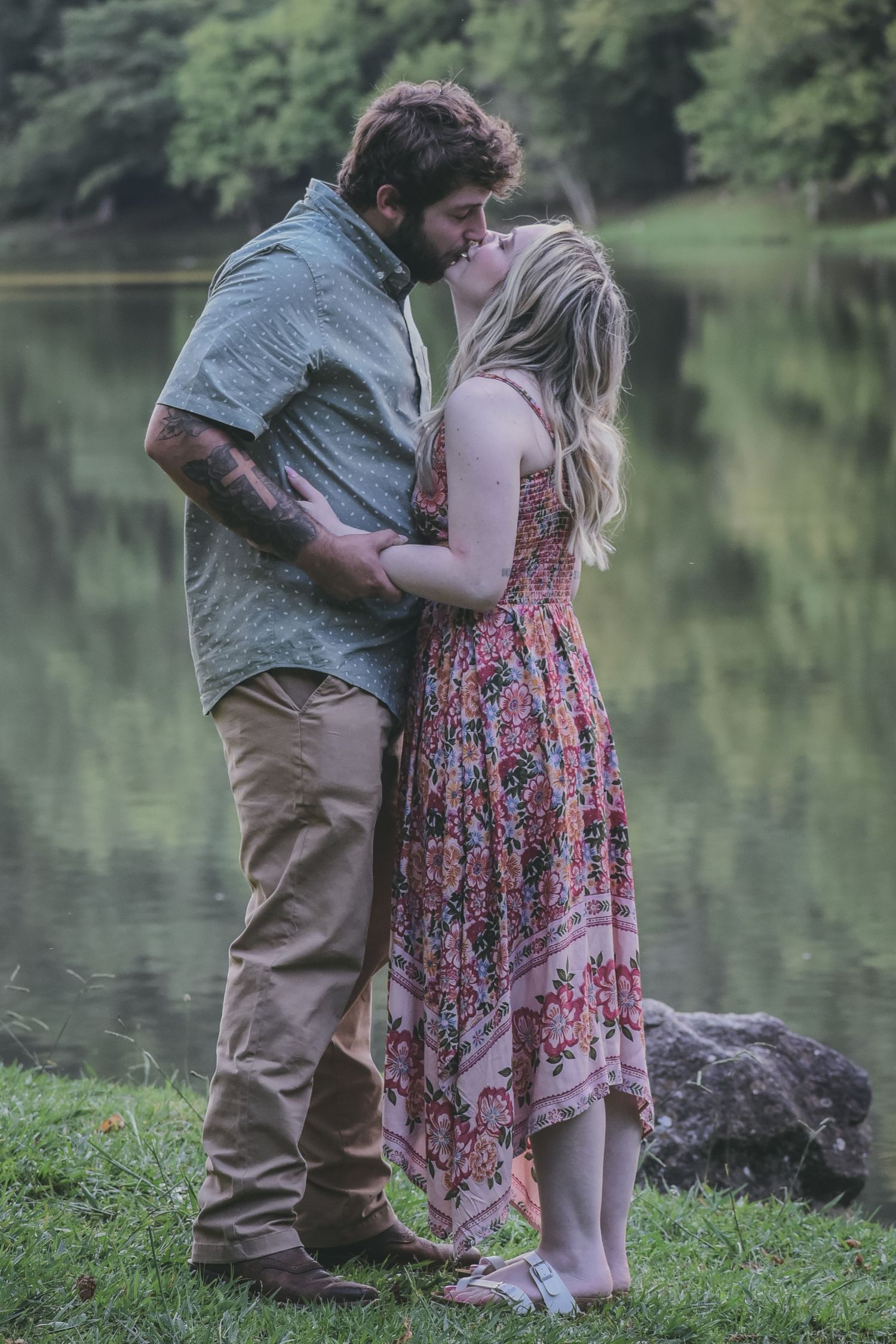 A romantic lakeside scene with a couple embracing on grassy shoreline.