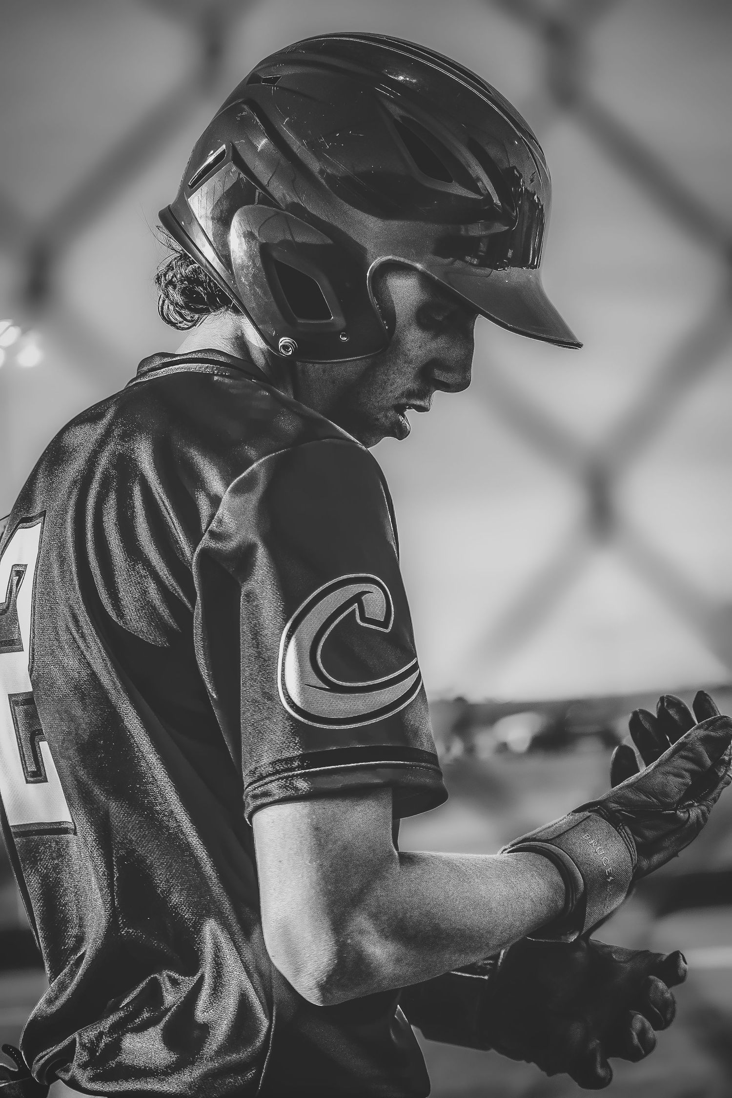 Black and white photo of a baseball batter in helmet and gloves preparing at the dugout fence.