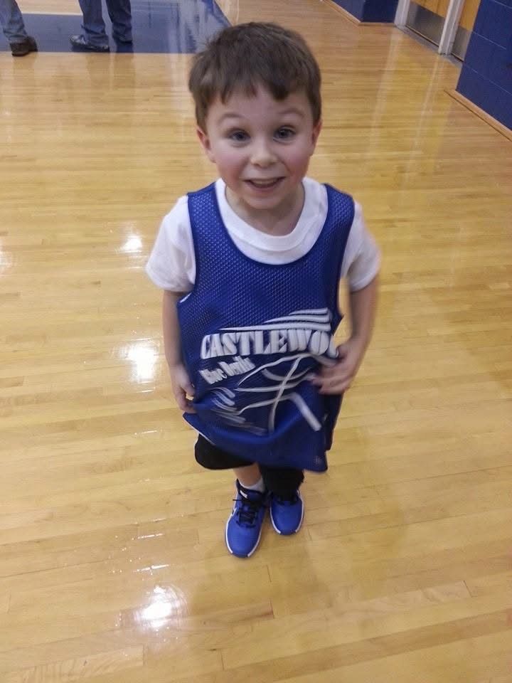 Young basketball player in blue jersey stands on shiny wooden court floor.
