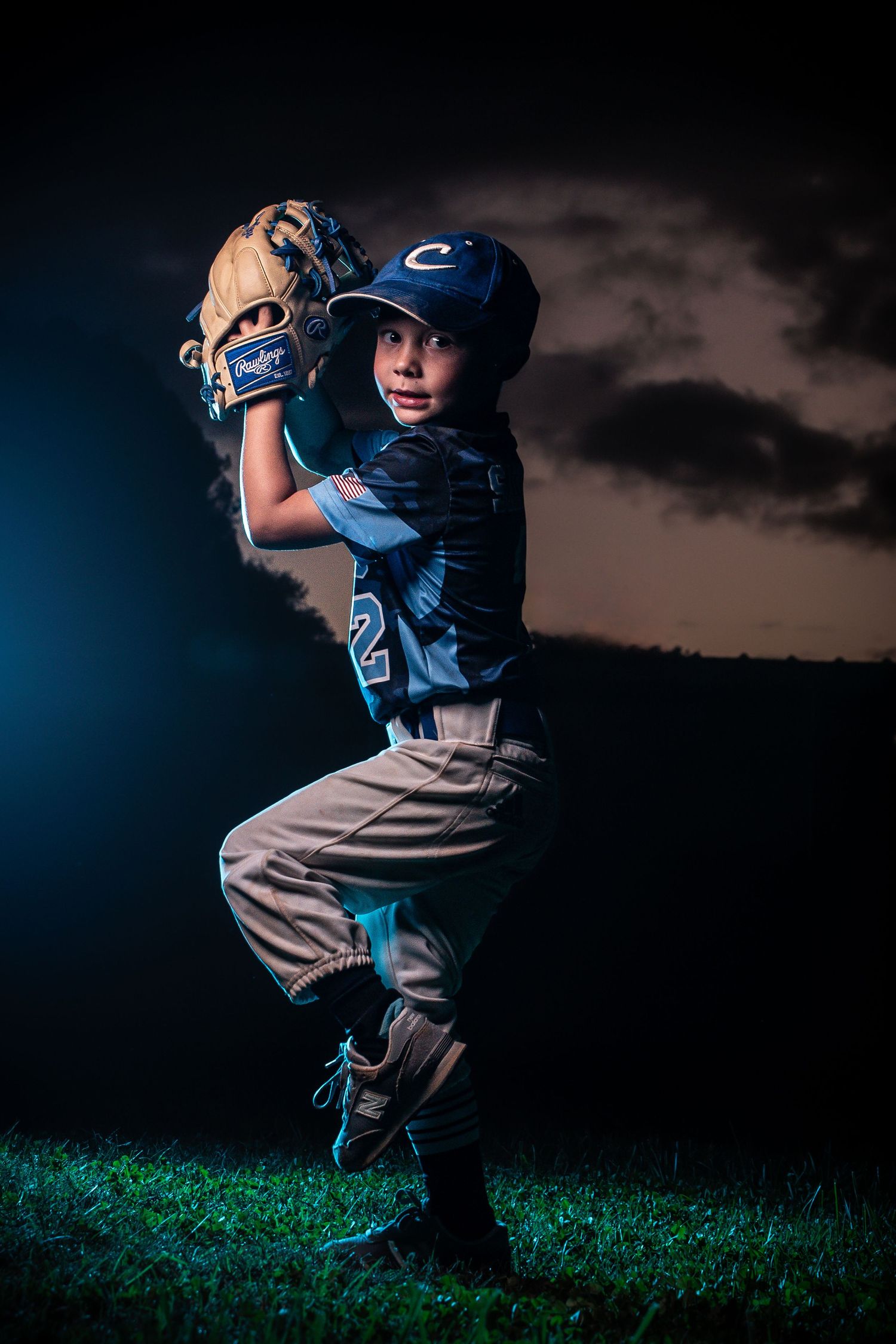 Youth baseball player in dramatic pose with evening sky backdrop.
