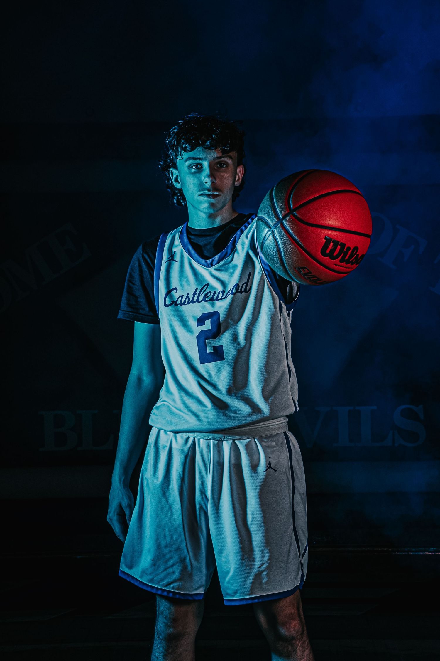 Basketball player in white uniform holds red ball against dramatic blue-lit backdrop.