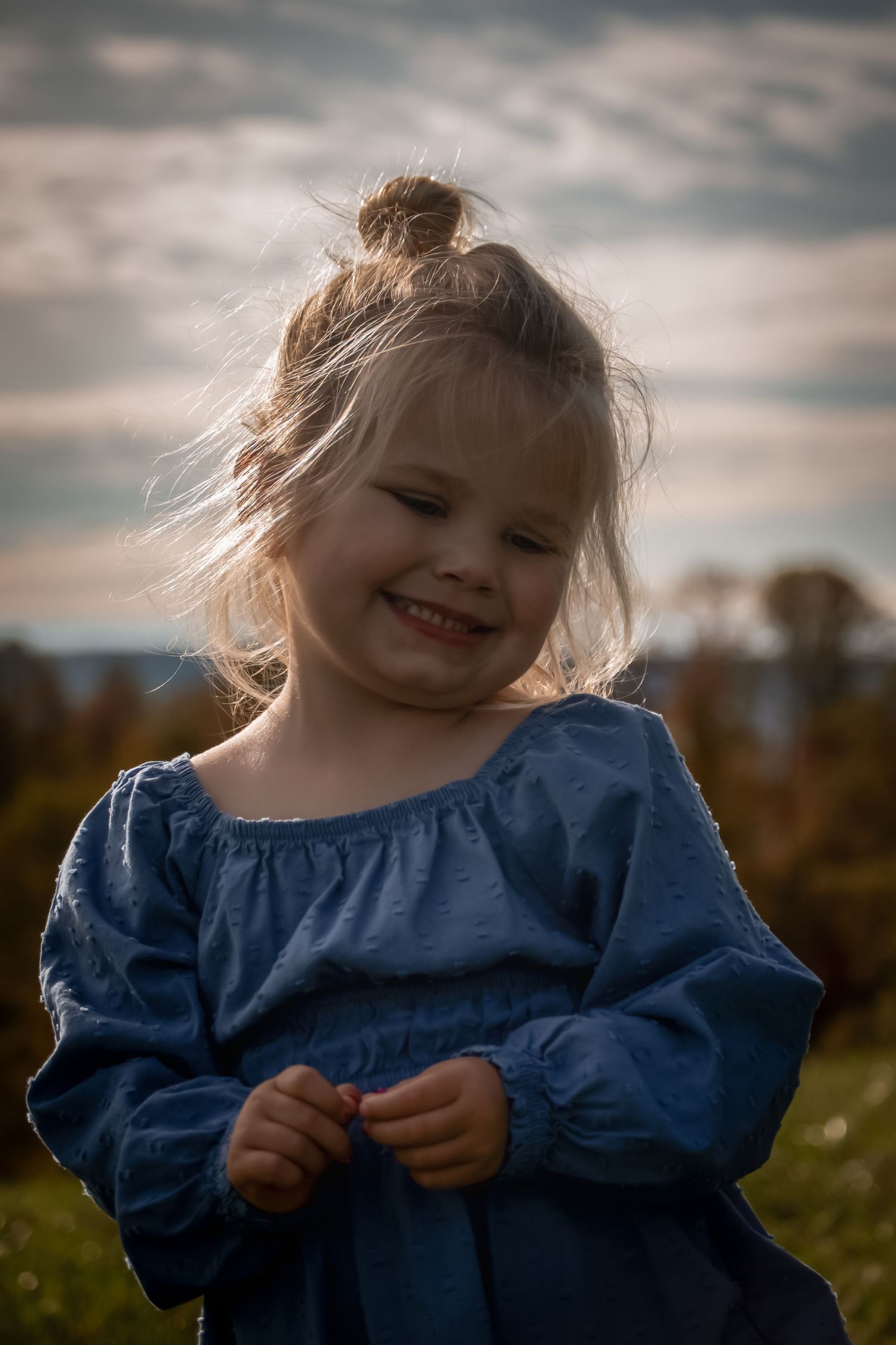 Candid moment of joyful laughter in autumn field wearing blue dress.