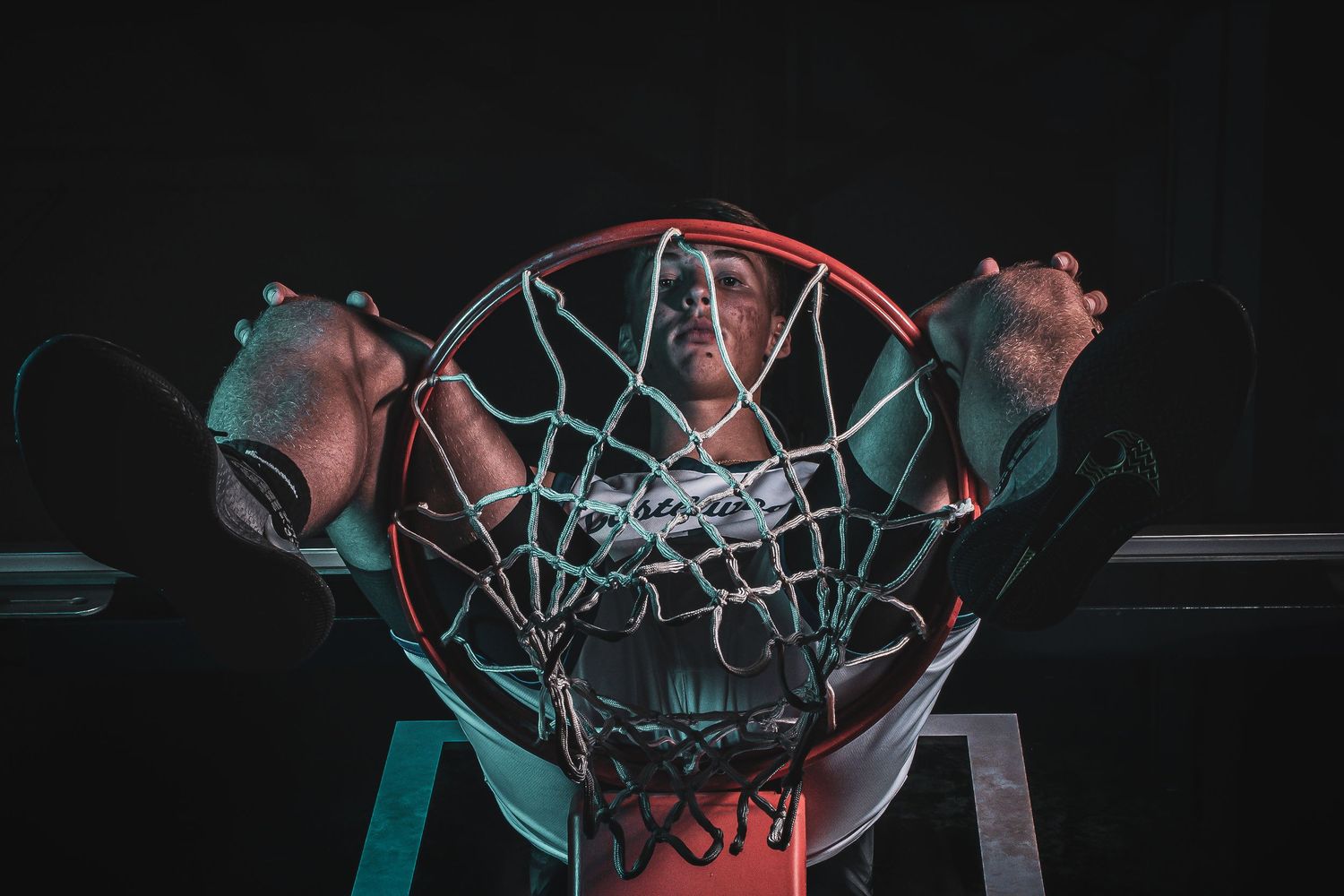 View through basketball net of player in dramatic lighting wearing Castlewood jersey.