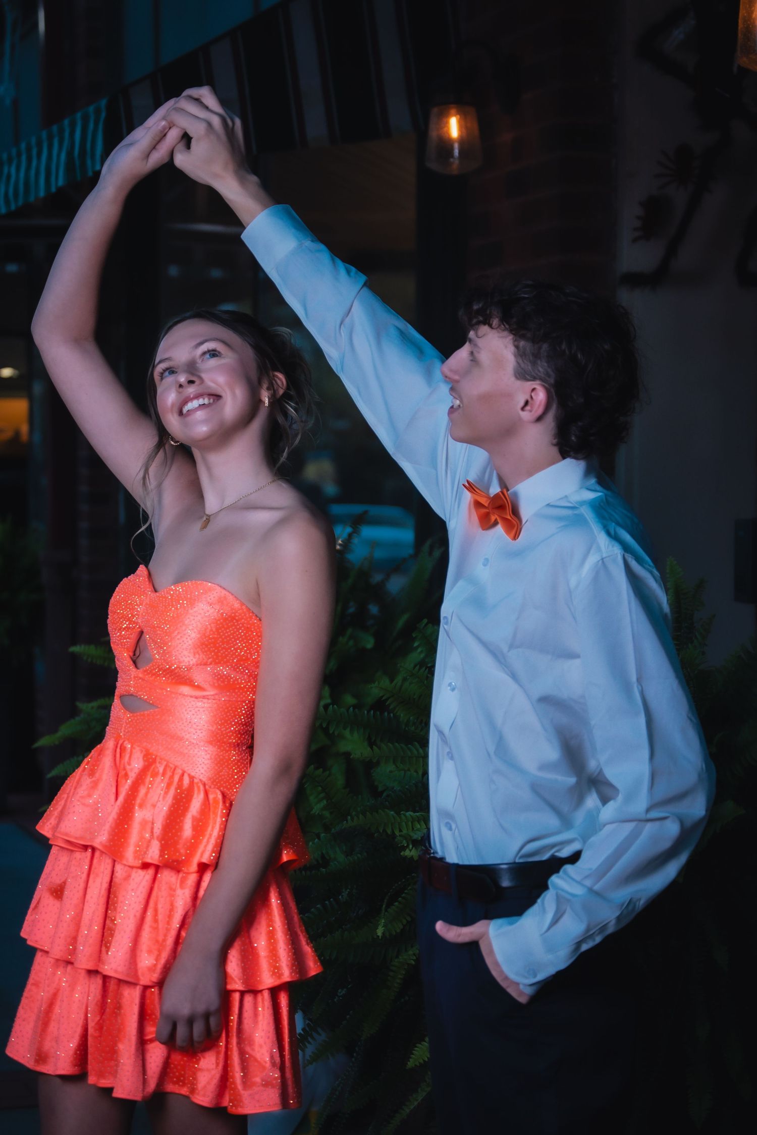 Couple dancing together at a formal event with one person wearing a bright coral dress and the other in a white dress shirt.