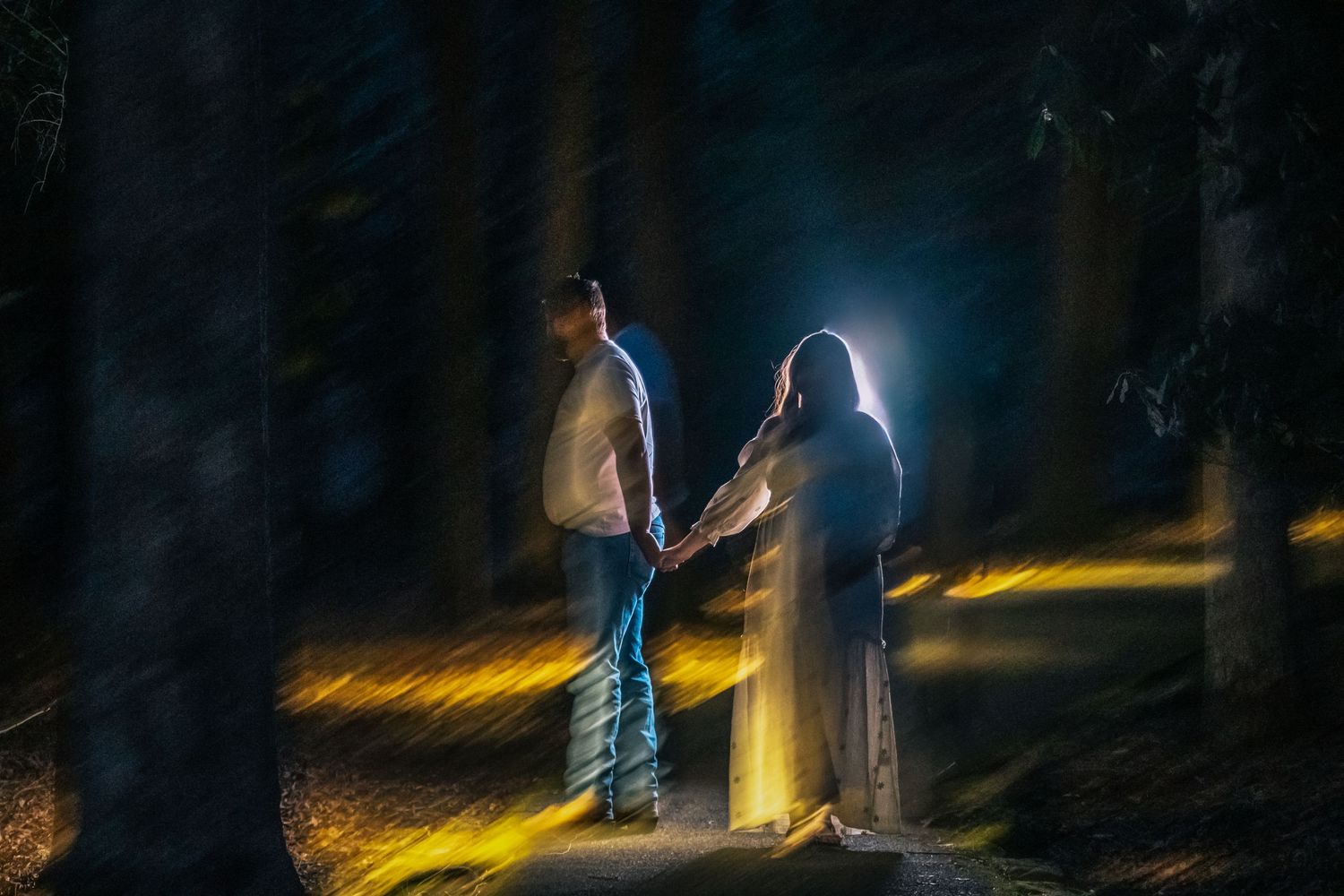 A person stands in a dark forest illuminated by a mysterious glowing yellow light creating an eerie atmosphere.