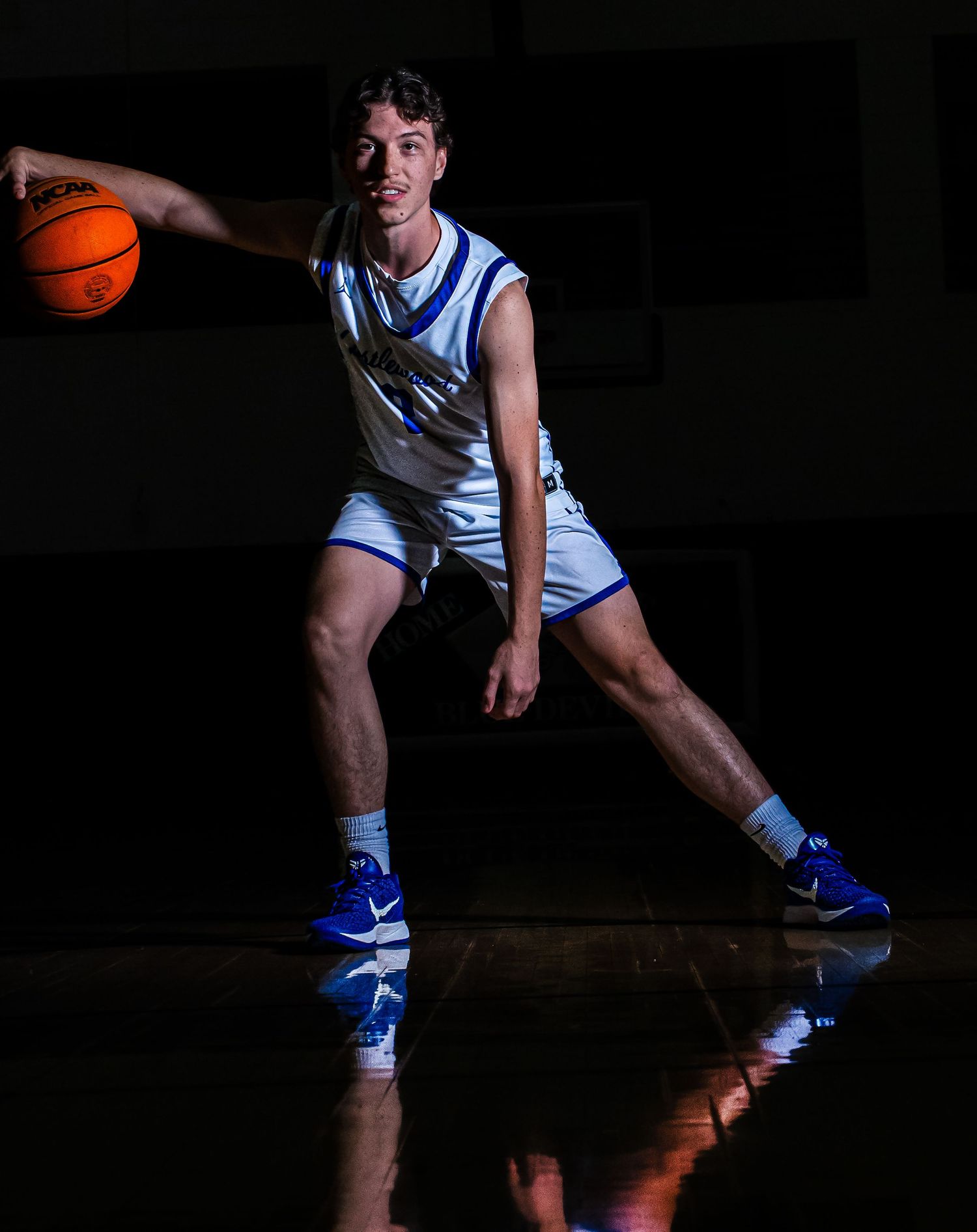 Basketball player in white and blue uniform demonstrates dribbling stance.