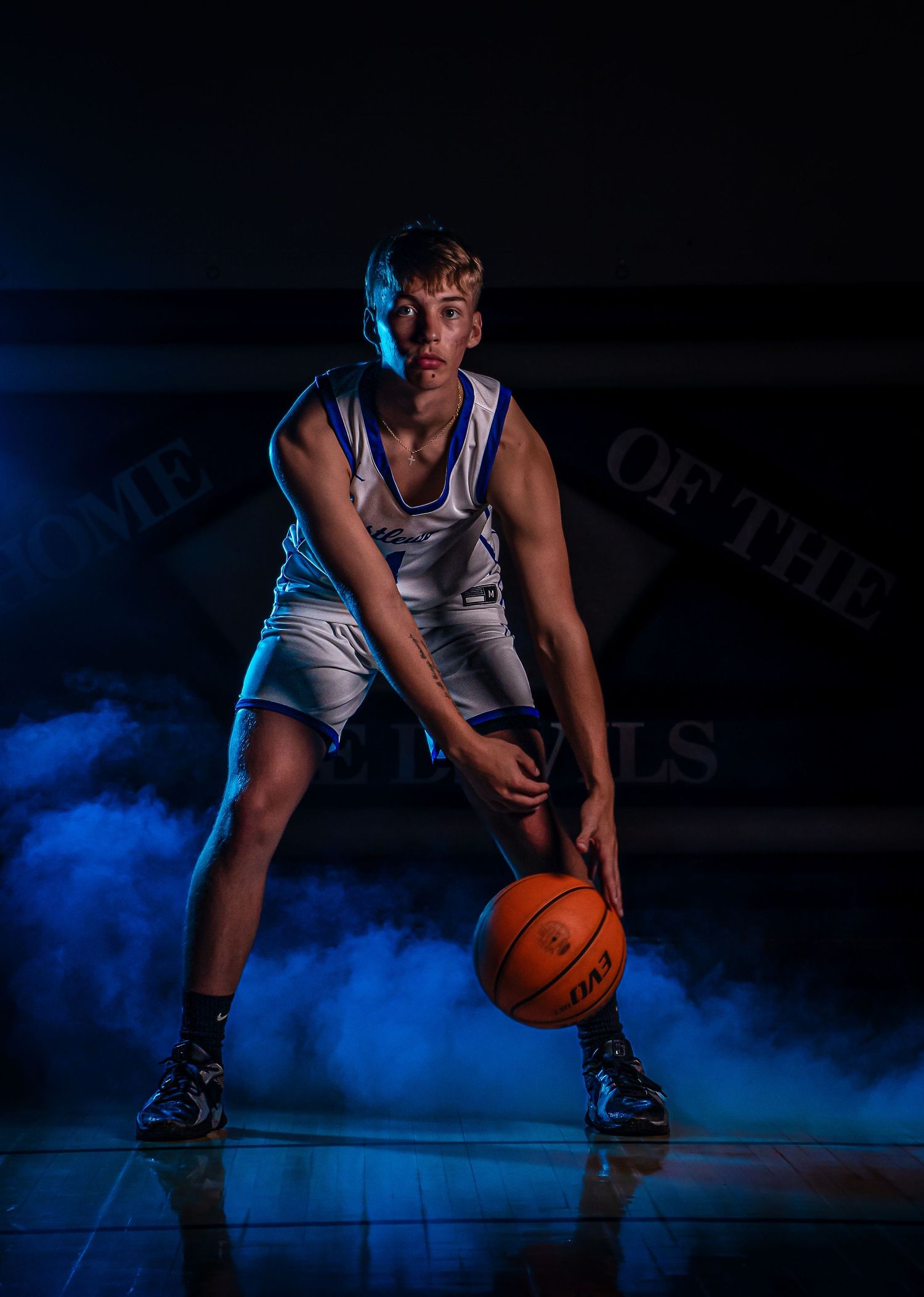Basketball player dribbles on hardwood court with atmospheric blue smoke effect.