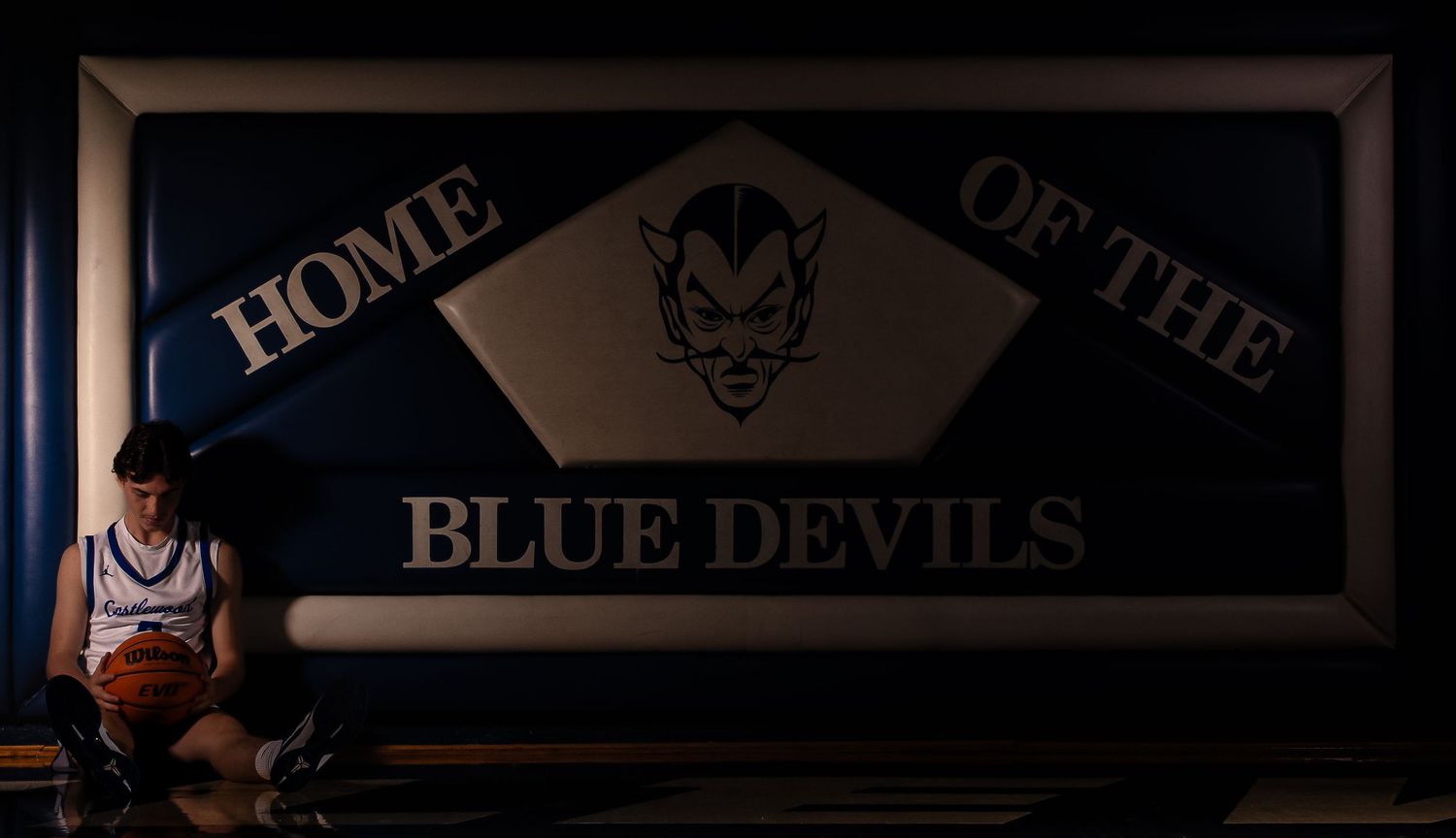 Athlete sits contemplatively under Blue Devils team banner in moody lighting.