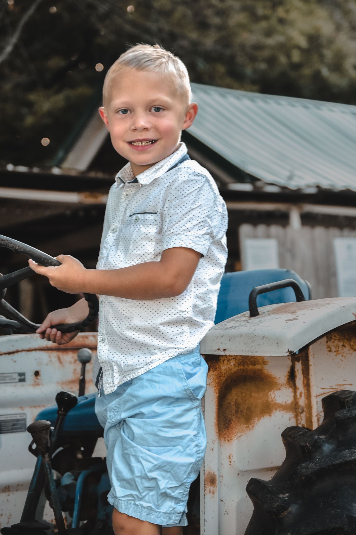 White polka dot shirt and light blue shorts against rustic farm equipment.