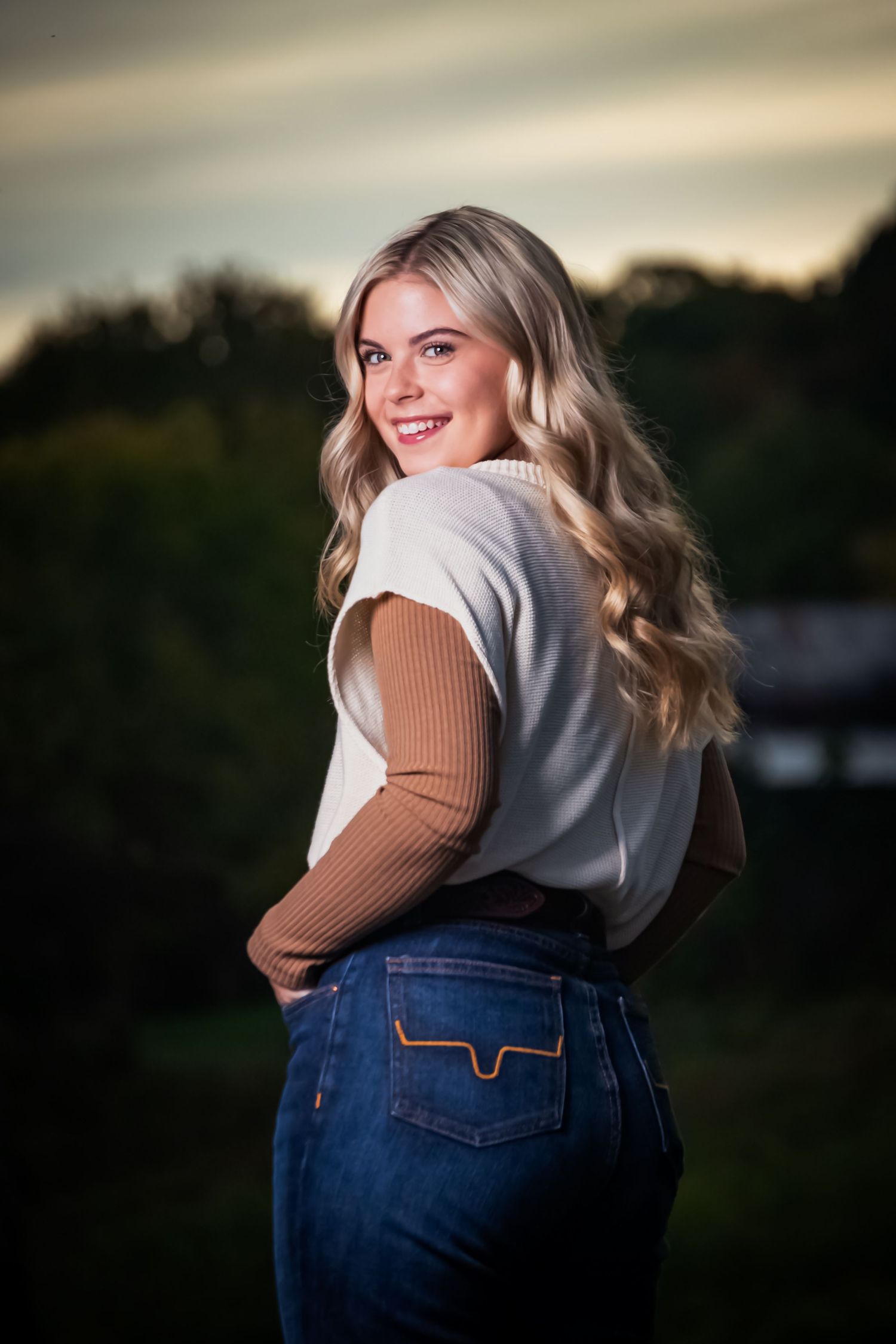 Stylish outfit featuring flared jeans and a two-tone top captured in golden hour lighting with a natural backdrop.