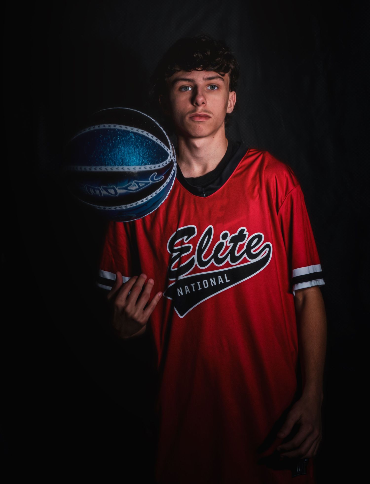 A basketball player in a red jersey poses with a basketball in a series of dramatic studio portraits.