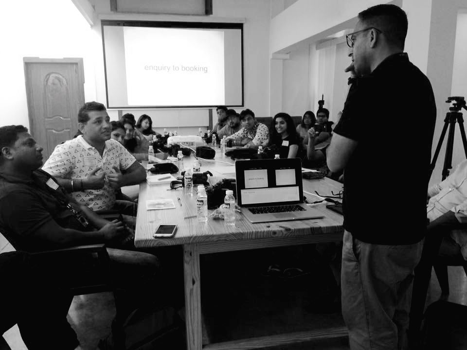 Business meeting participants gather around a conference table in a modern office setting.