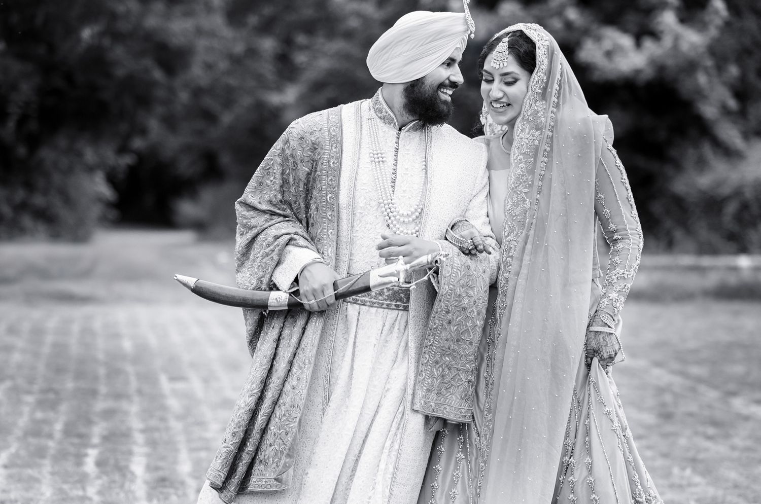 Black and white photo of couple in traditional Sikh wedding attire walking together.