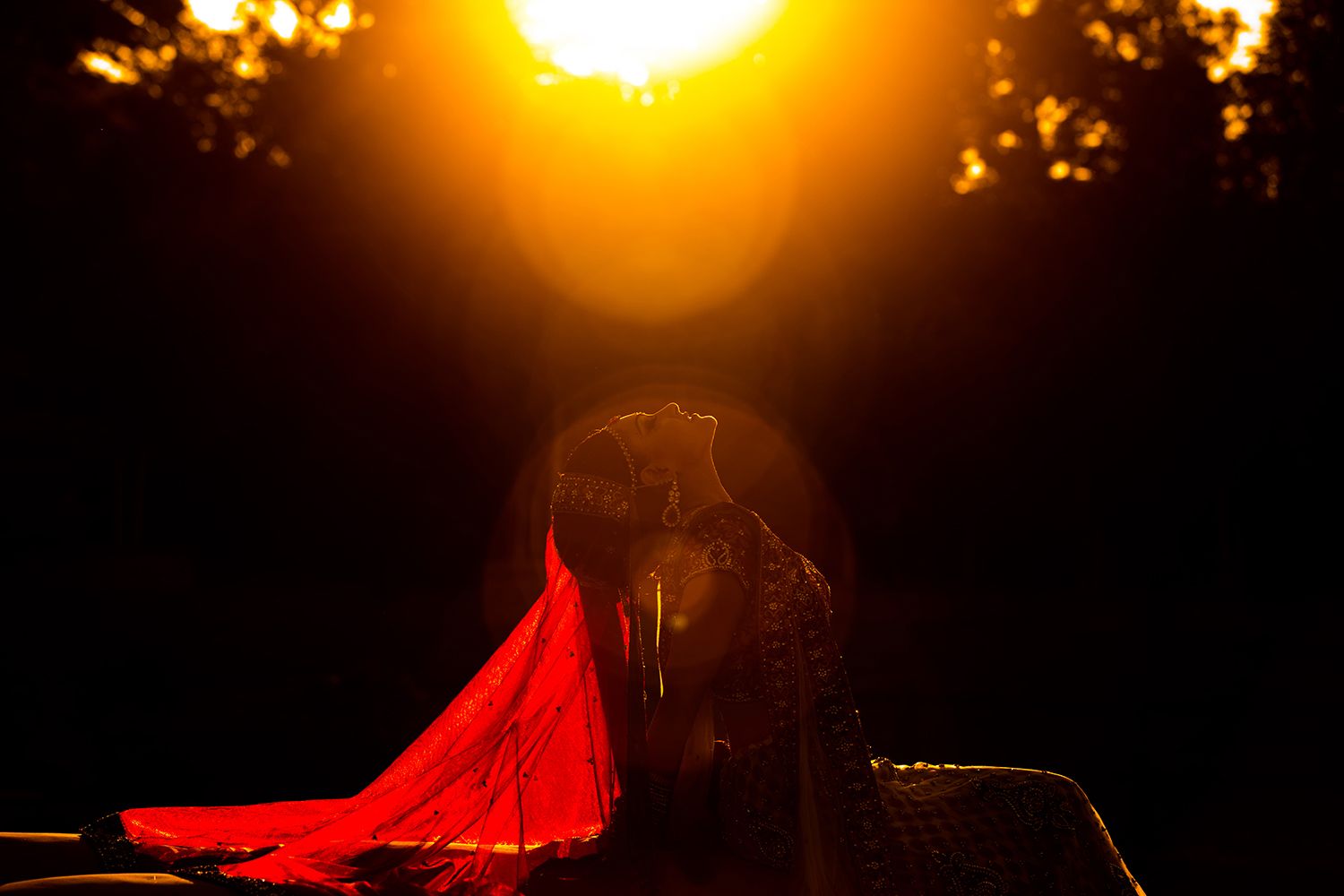 Dramatic sunset silhouette with flowing red dress against golden sky.