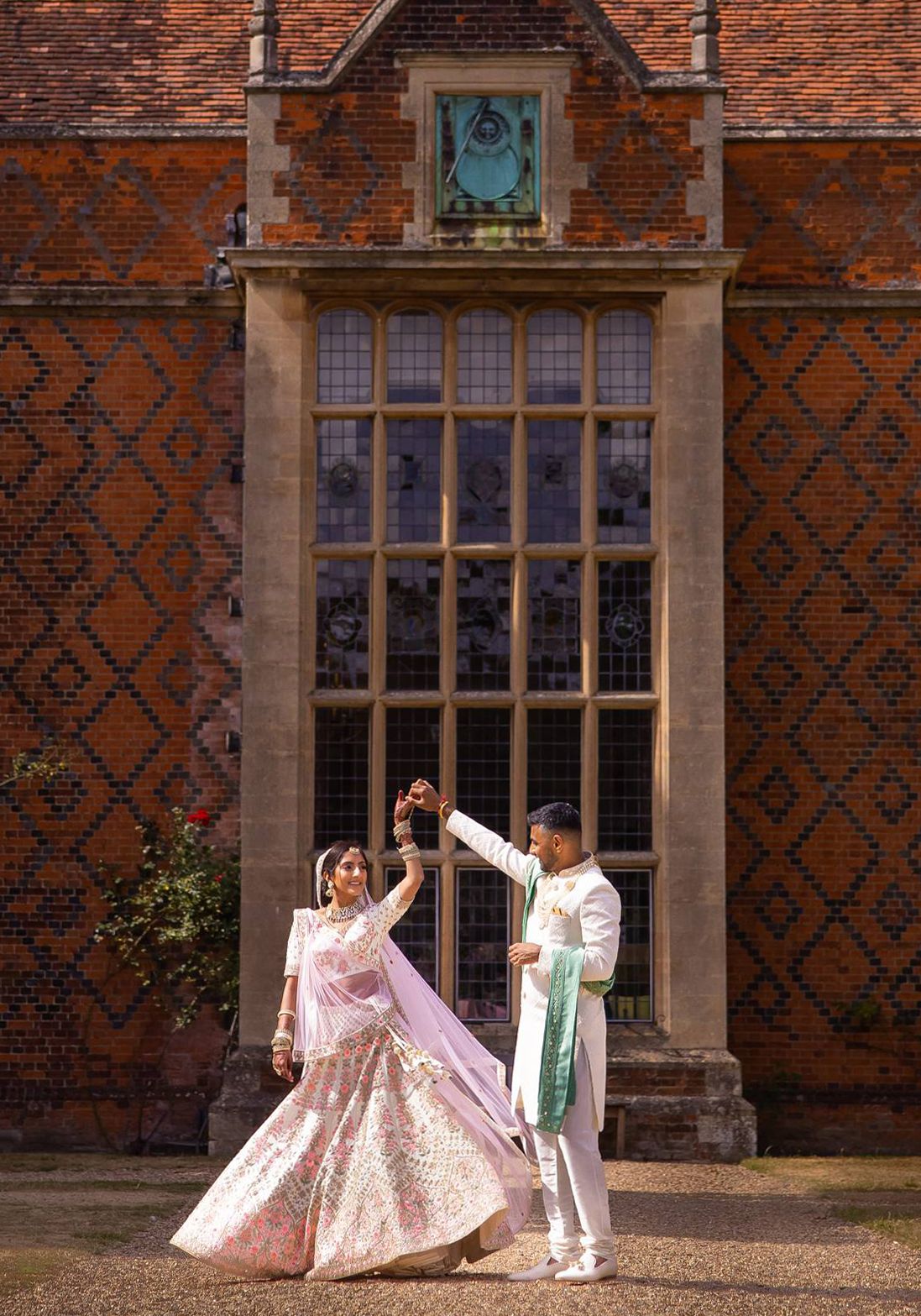 Couple in traditional Indian attire posing against historic brick building with elegant windows.