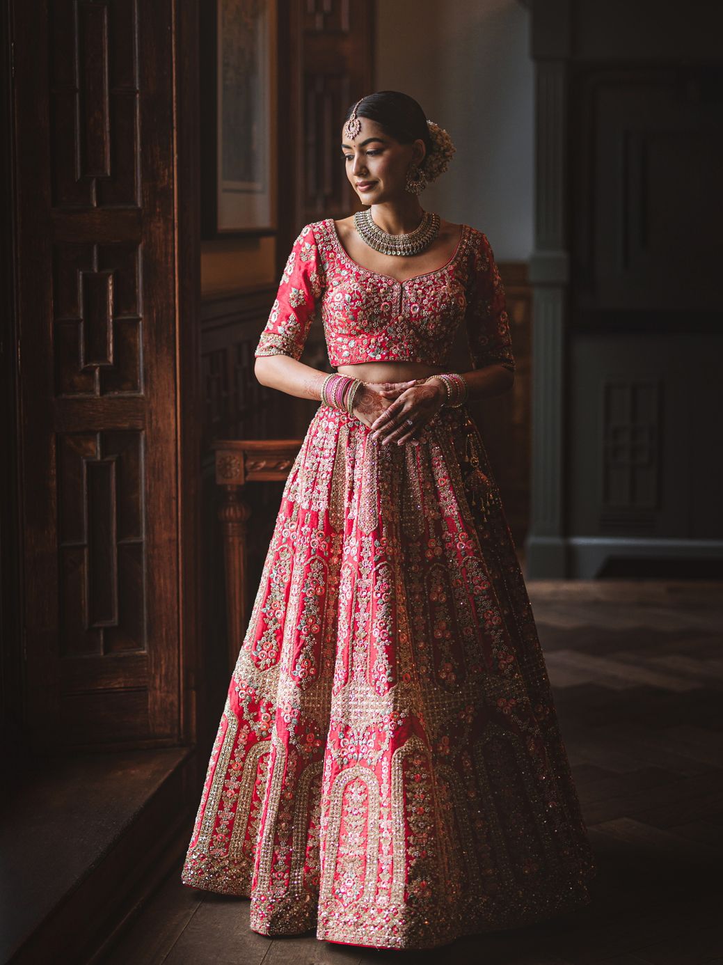 Elegant red and gold embroidered lehenga displayed in warm interior lighting.