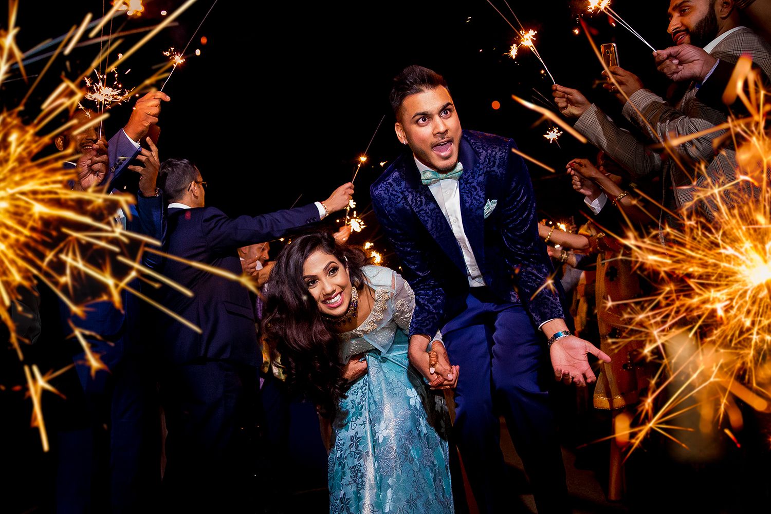 Wedding party celebrating with sparklers creating trails of light against dark night sky.