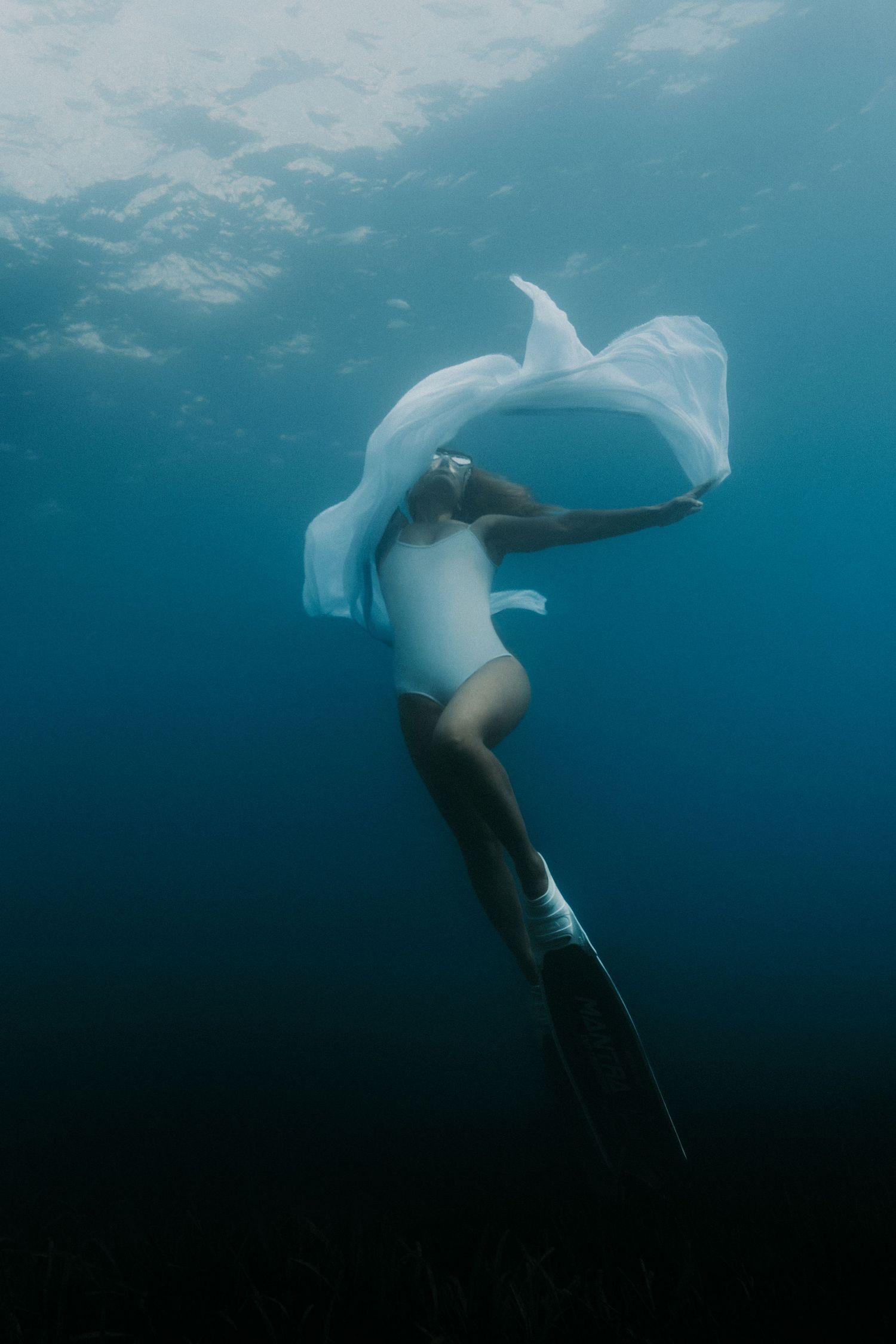 Ethereal underwater dance performance with flowing white fabric in deep blue waters.