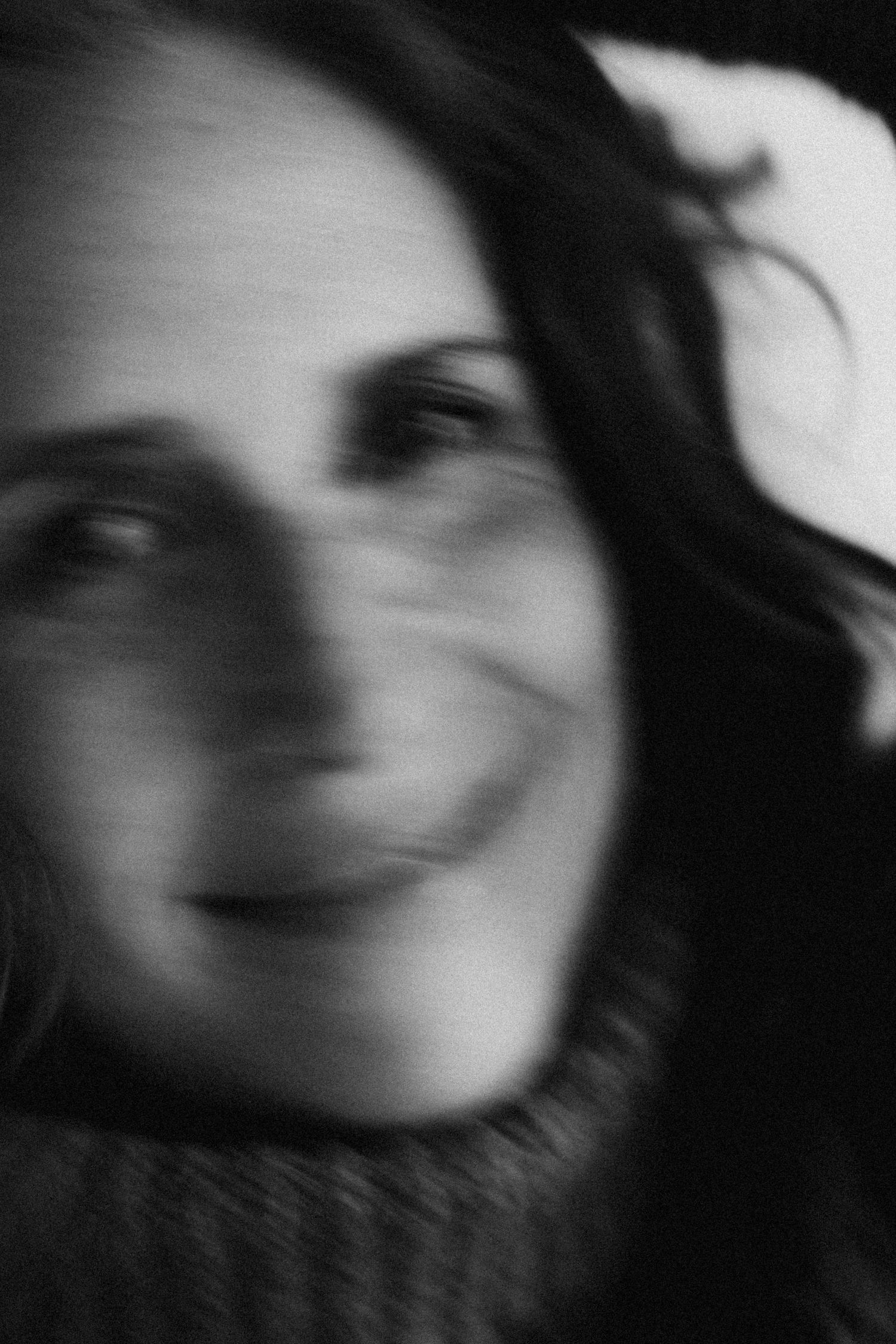 Black and white blurred portrait of a smiling woman with dark wavy hair wearing a turtleneck sweater.