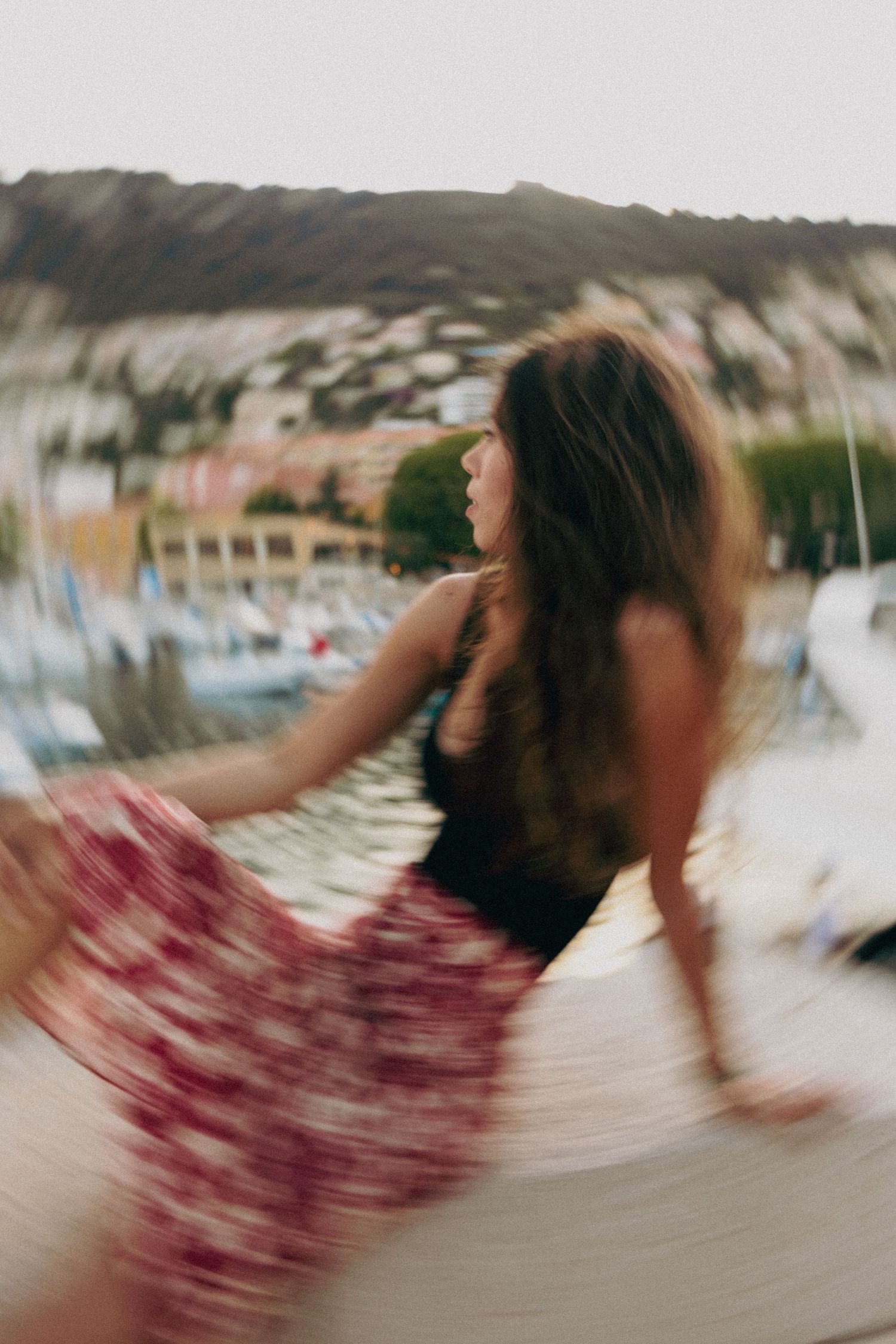 Motion-blurred photo of someone twirling in a dress by a marina at sunset.