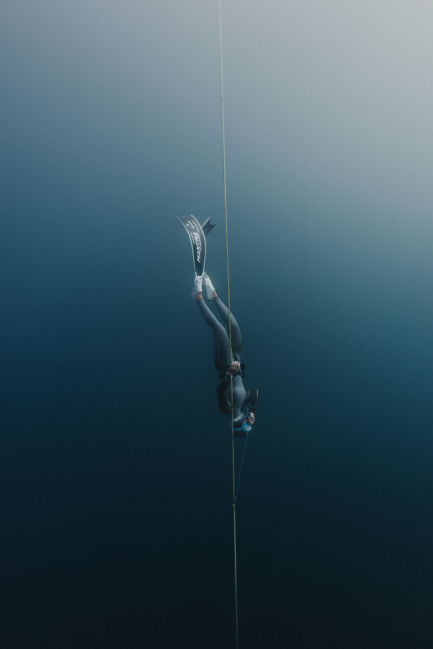 A freediver in a wetsuit descends along a guide rope into the deep blue ocean depths.
