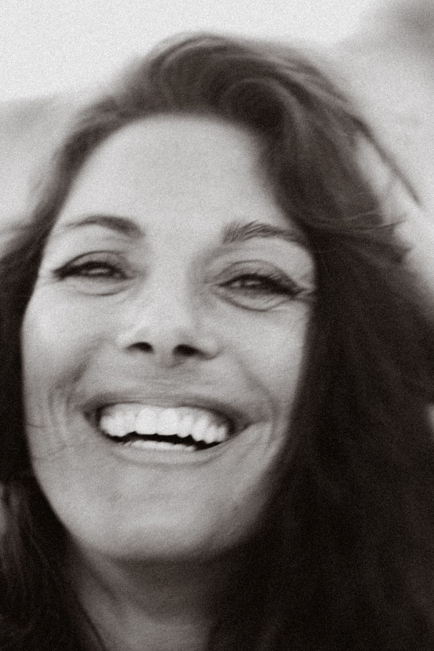 Black and white close-up portrait of a smiling woman with dark hair, captured in a candid moment.