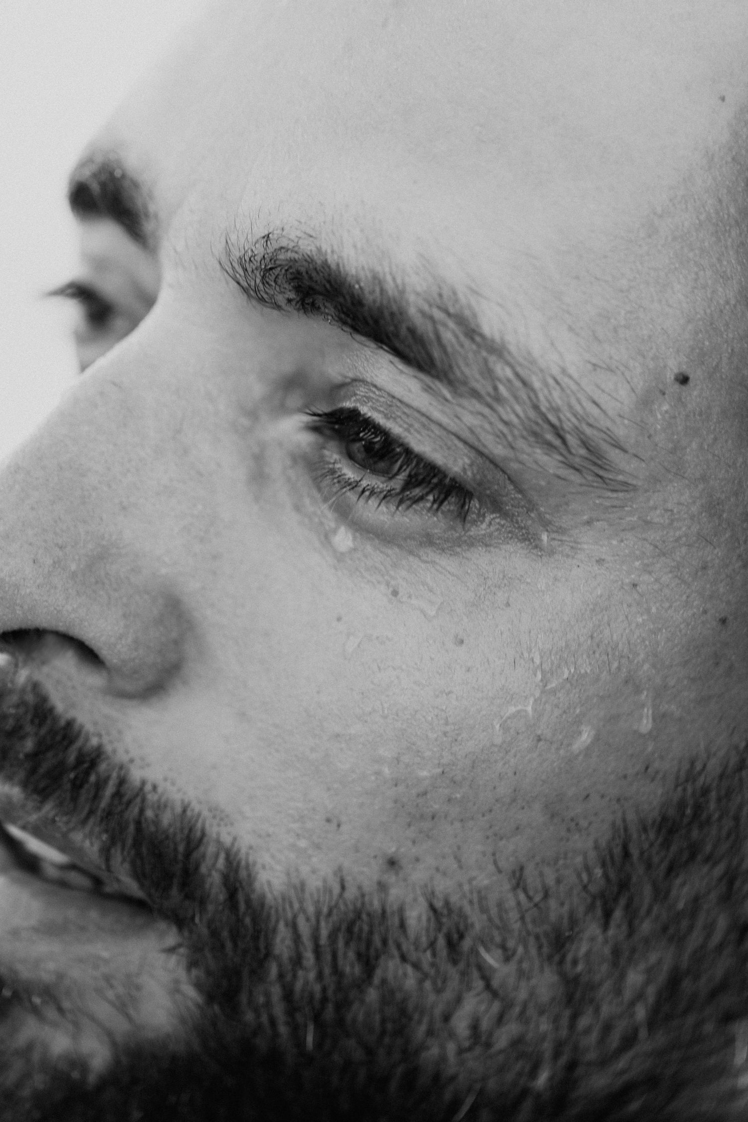 Close-up black and white photo of facial features showing beard stubble and partial profile view.