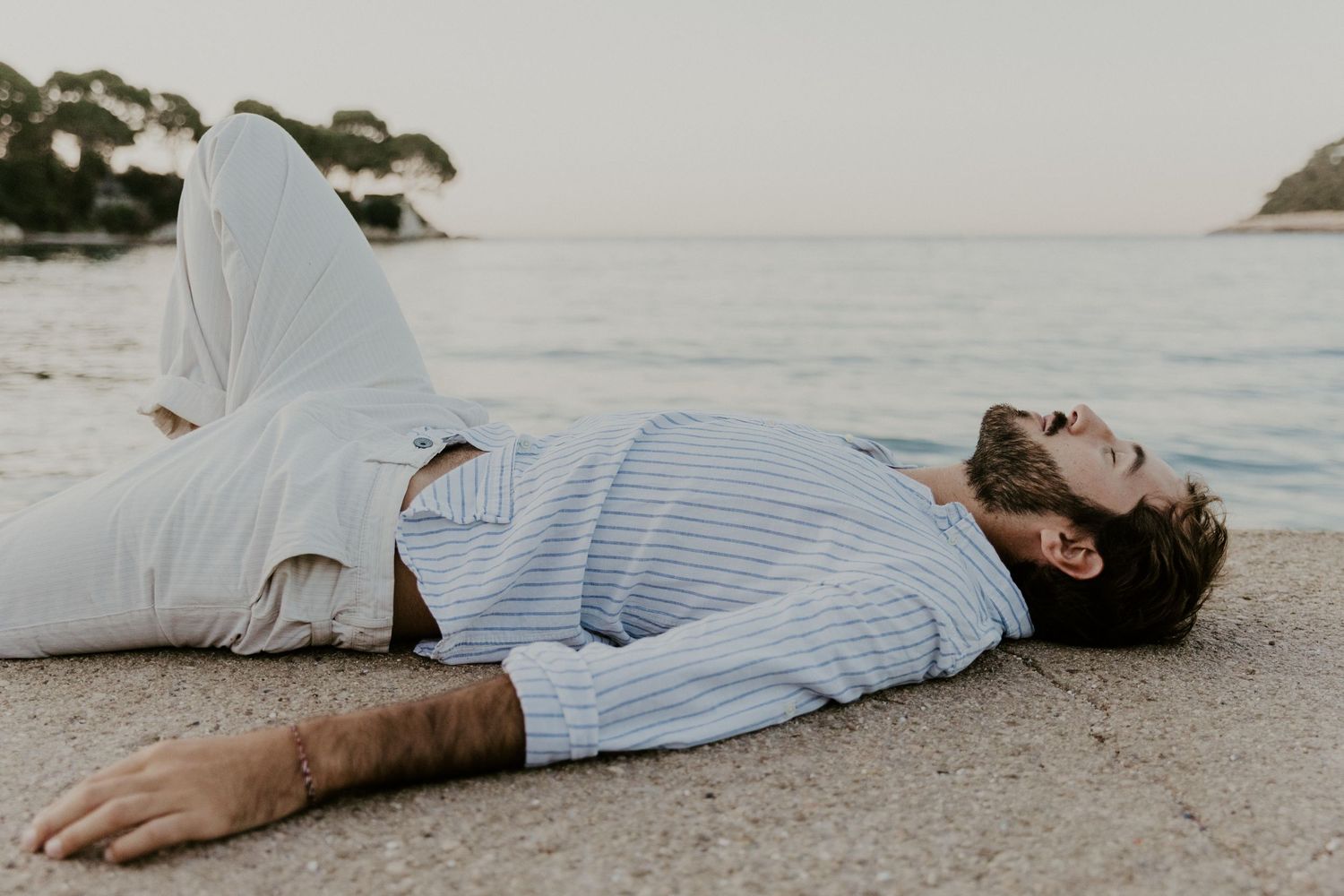 Person lying on beach shore in casual attire during sunset.