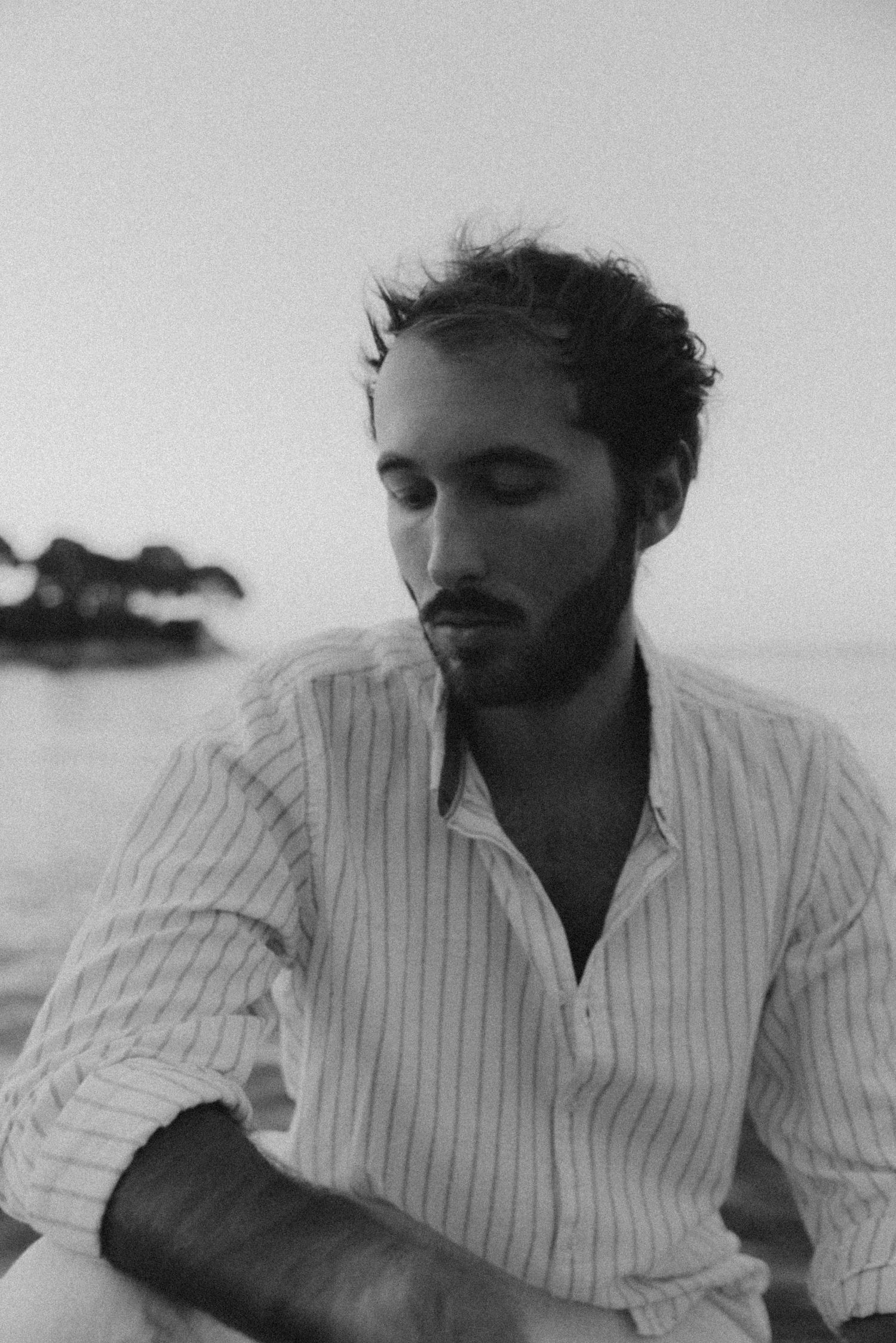 Artistic black and white portrait of person in striped shirt near water.