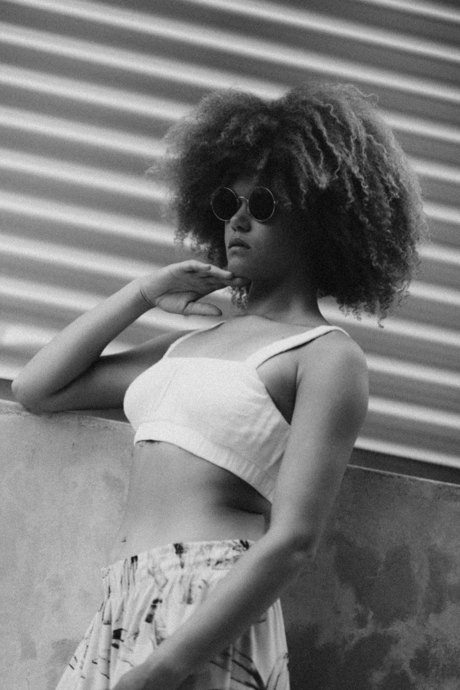 Artistic black and white portrait with sunglasses against industrial wall.