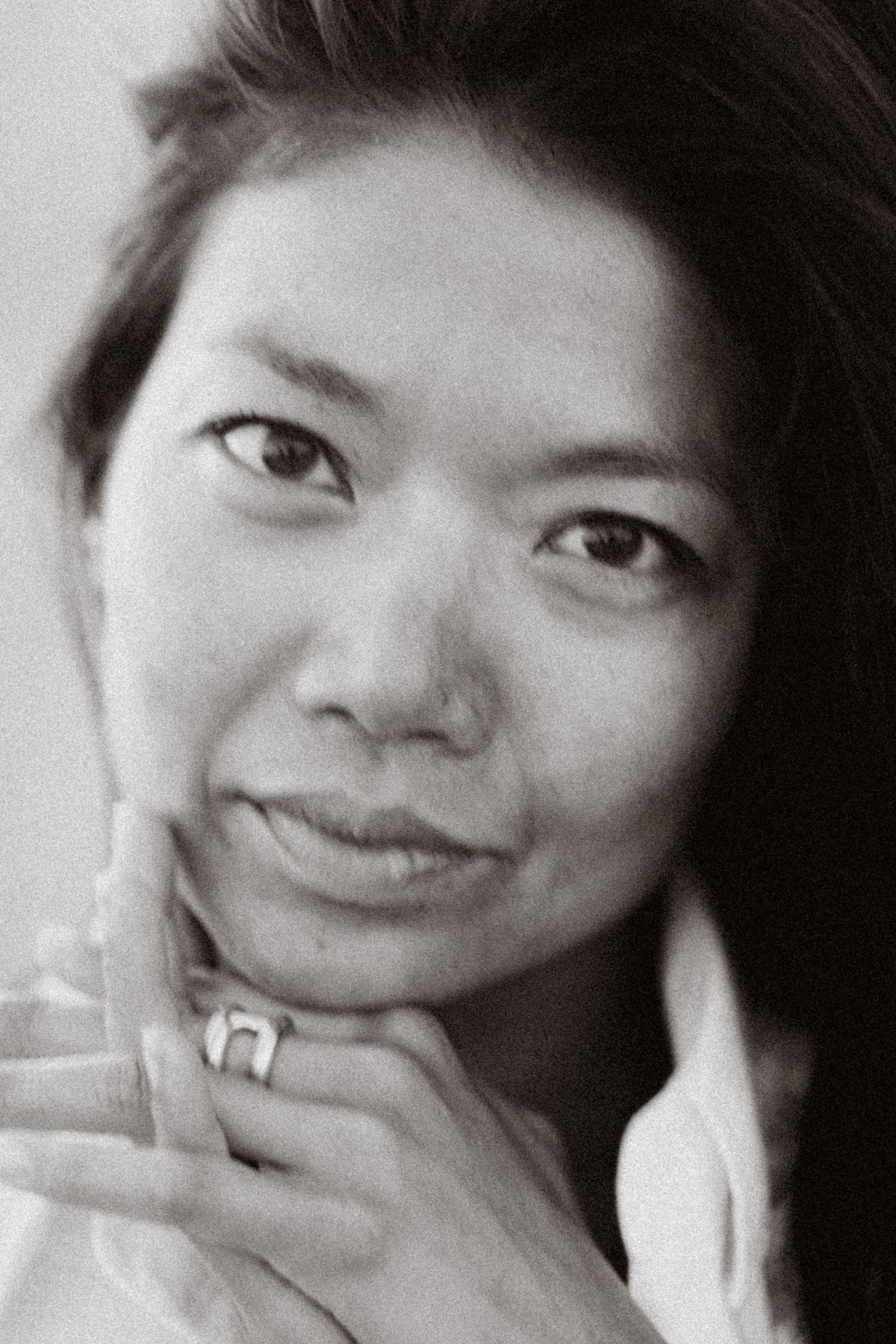 Black and white close-up portrait of a young Asian woman resting her chin on her hand, wearing a ring.