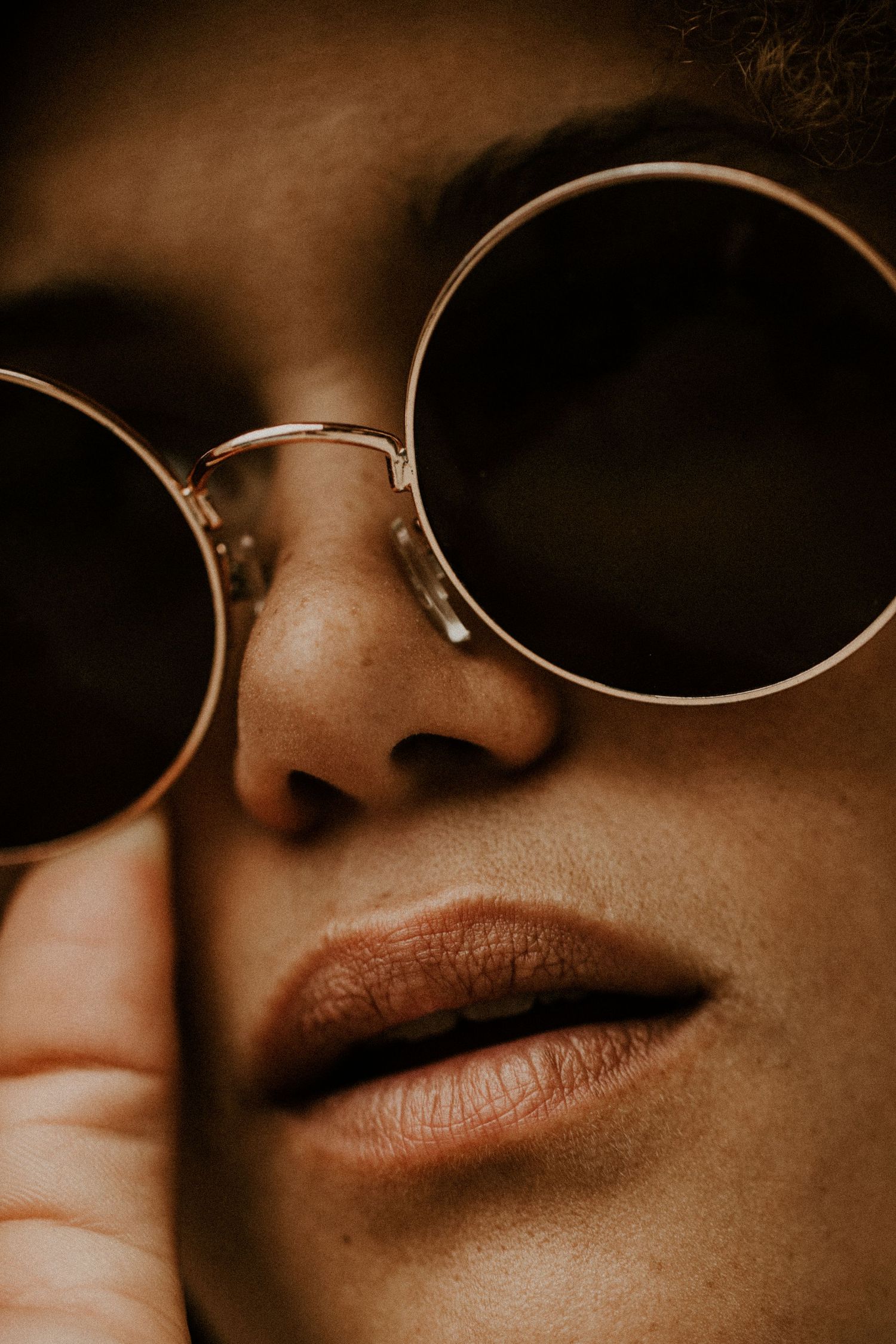 Sepia-toned extreme close-up of round sunglasses and lips creating artistic composition.