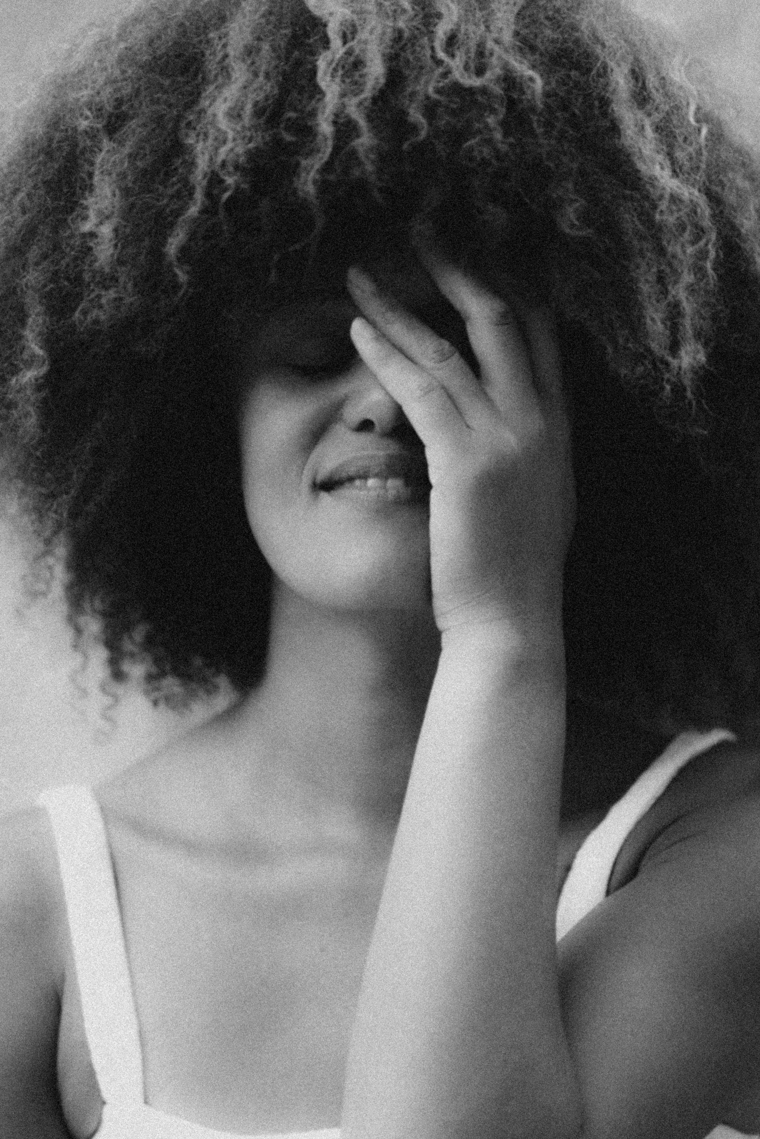 Intimate black and white portrait showing natural curly hair and playful hand gesture.