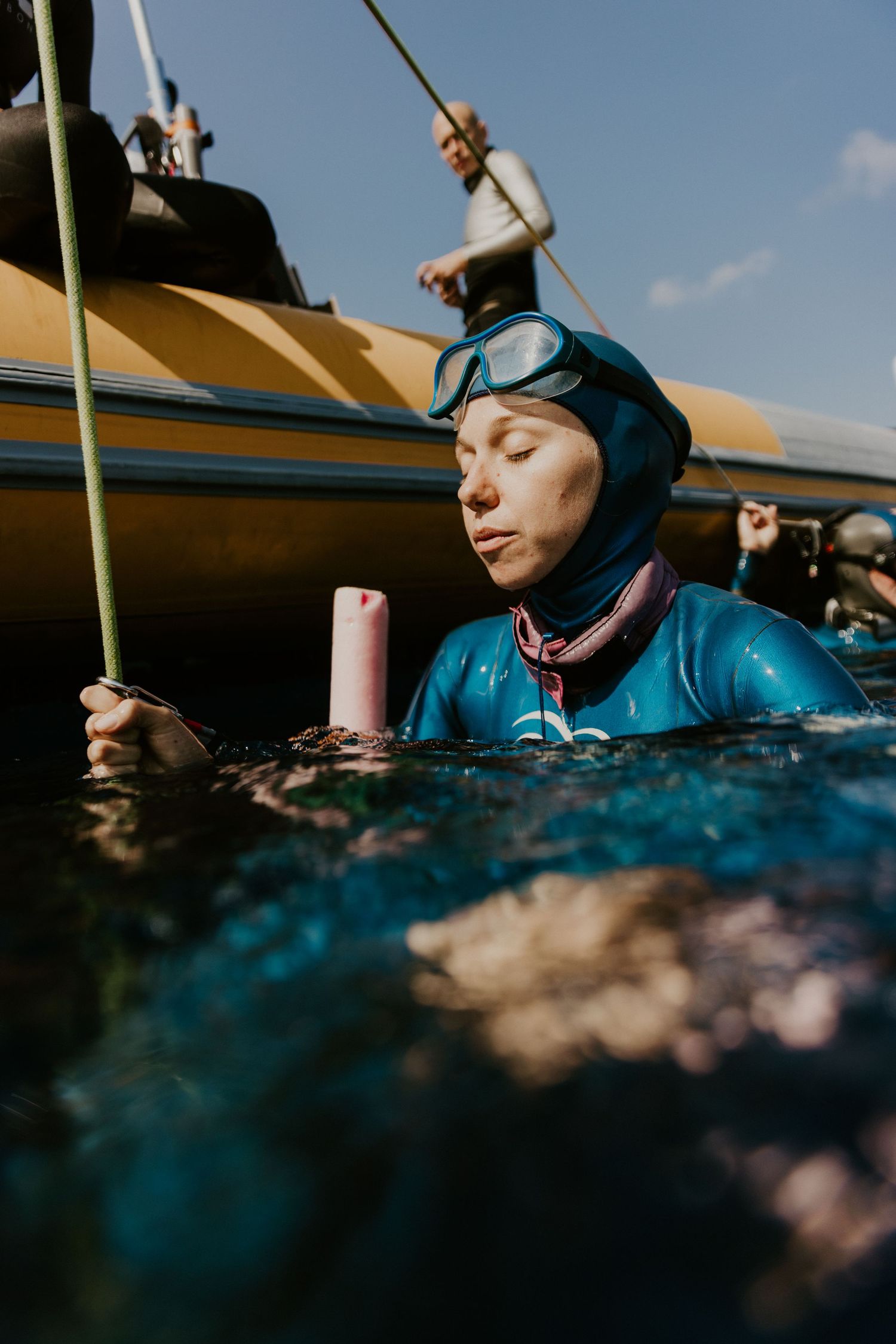 Diver in wetsuit preparing equipment near boat on sunny day.