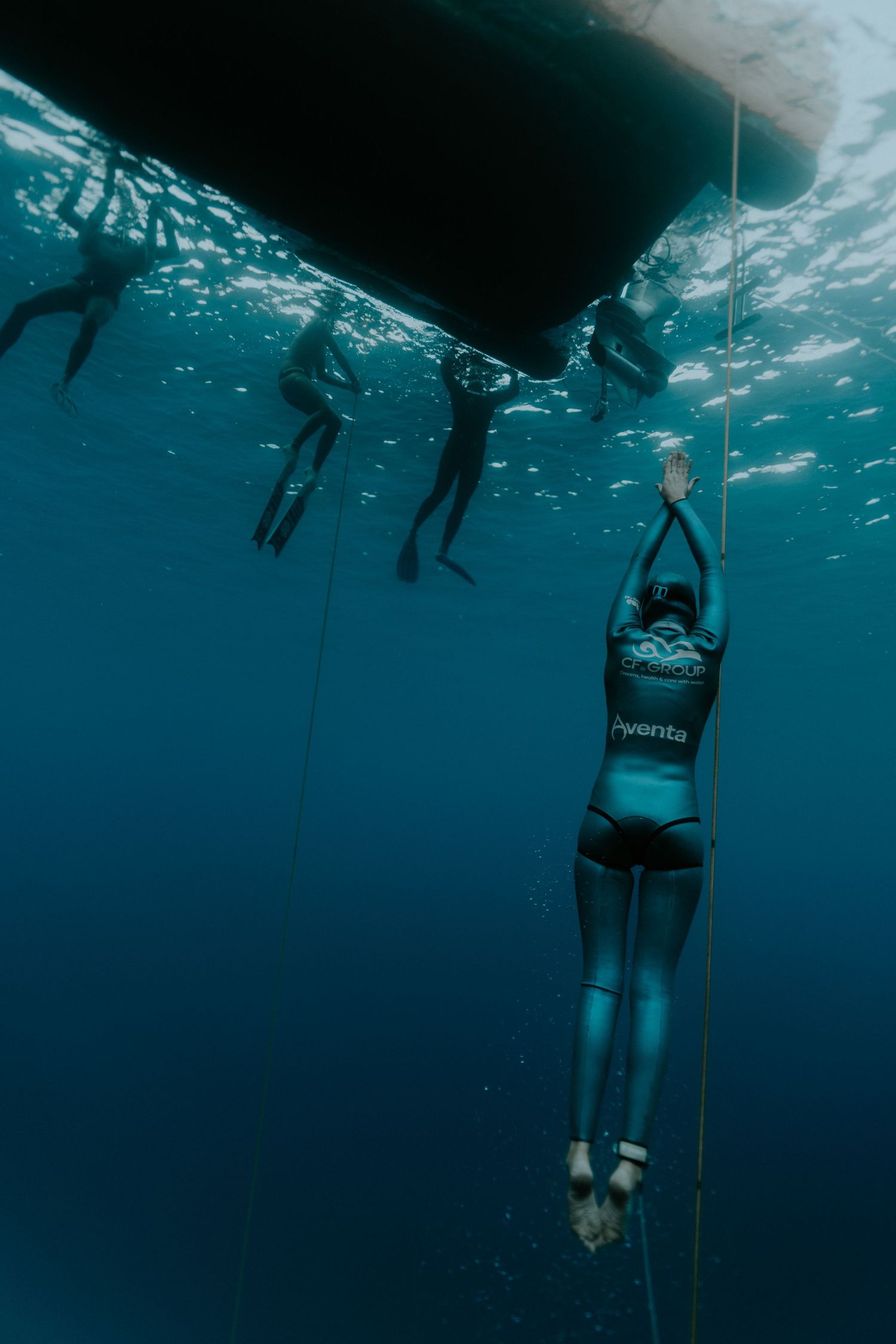 Multiple freedivers practicing underwater rope training in blue ocean waters.