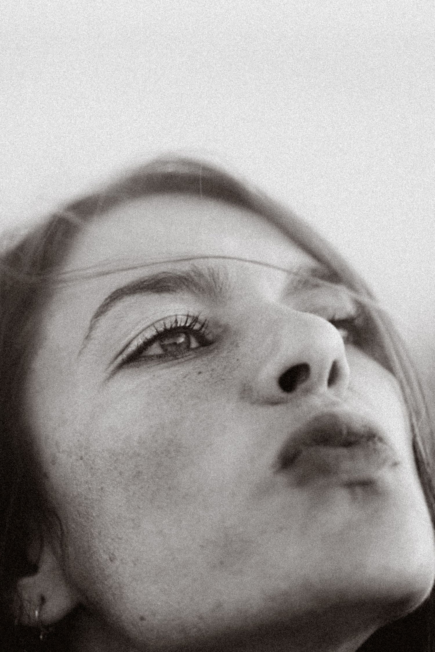 Black and white close-up portrait of a young woman with freckles gazing upward, showcasing natural beauty.