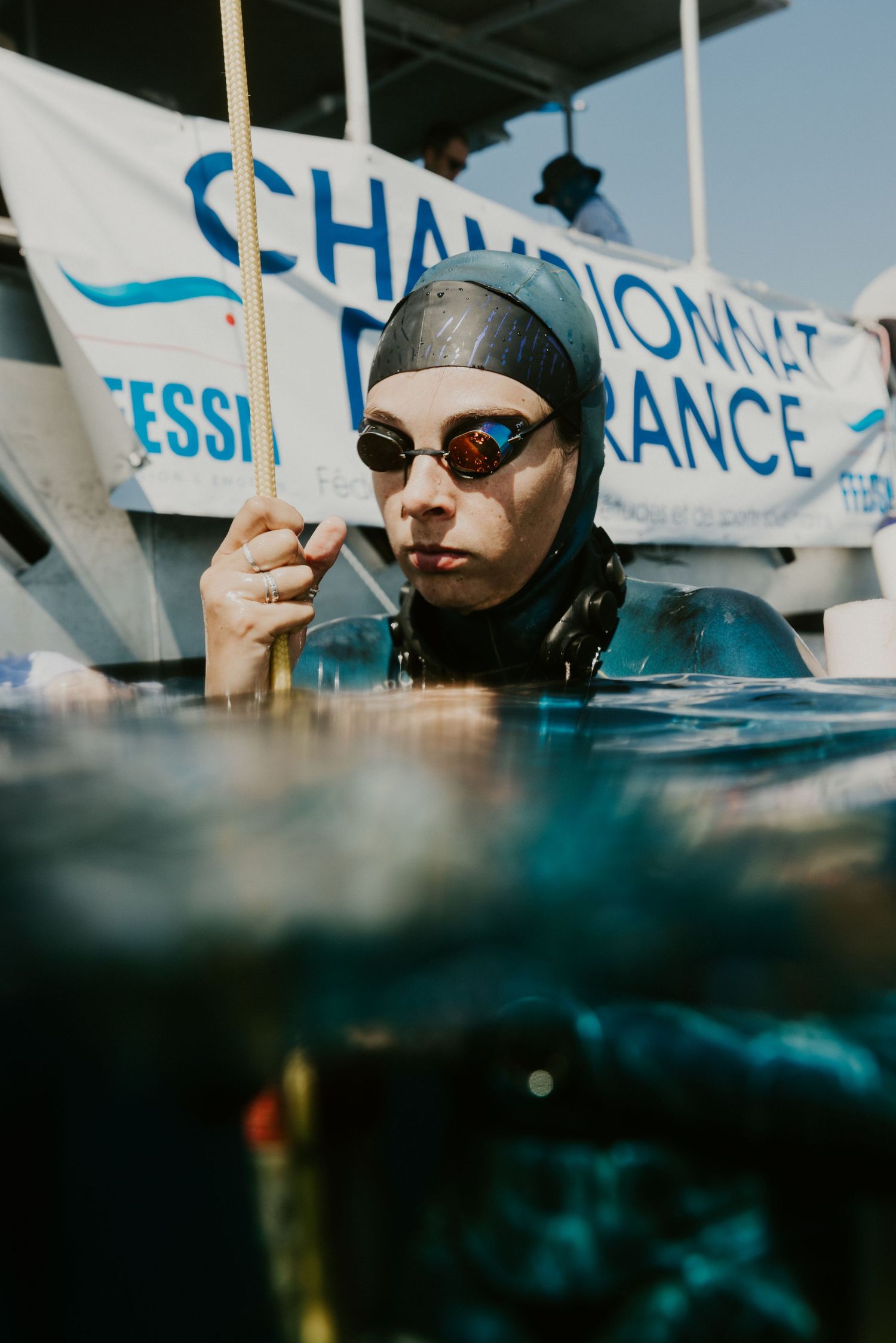 Freediver in wetsuit and goggles at Championnat de France competition, holding a rope at water surface.