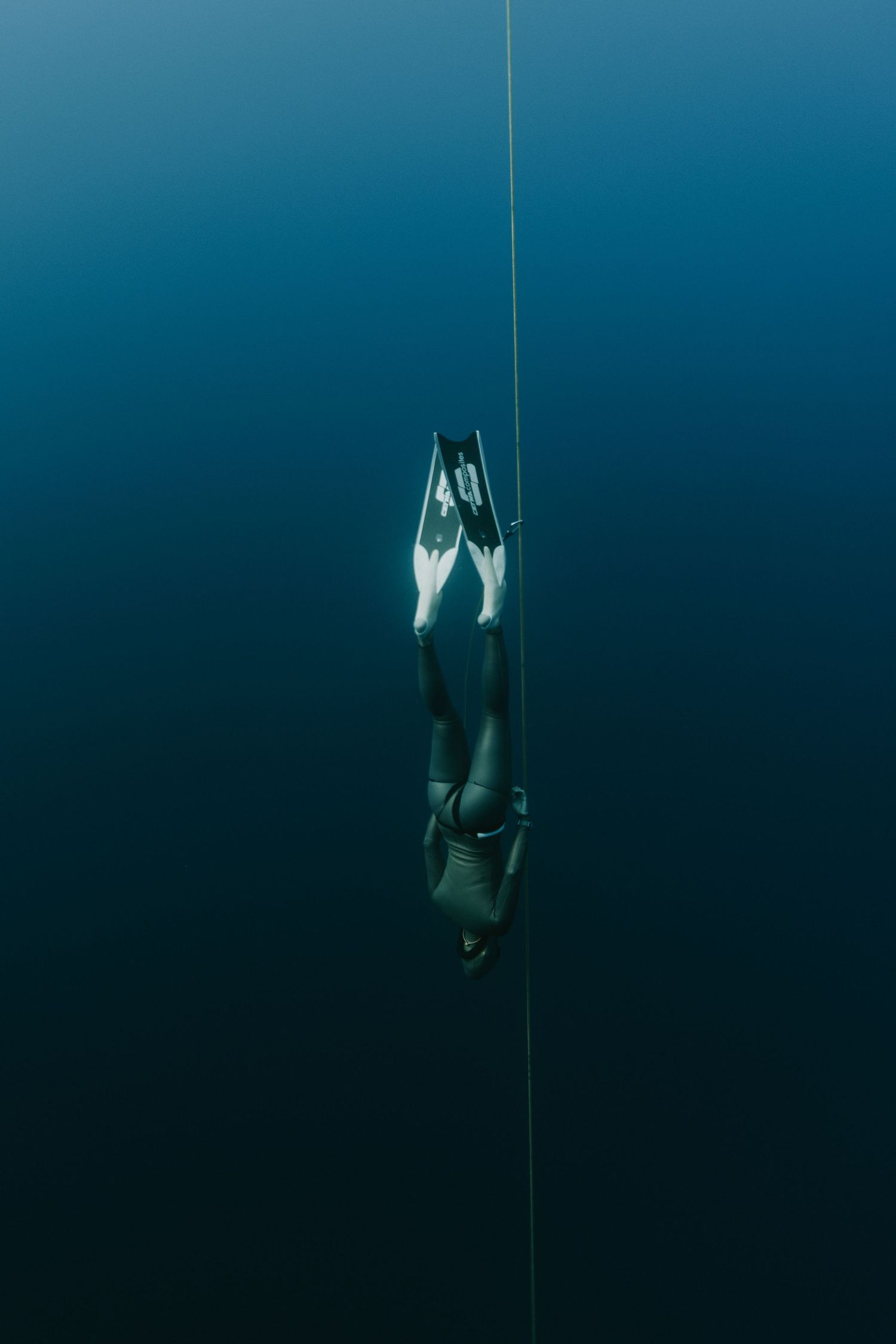A sequence of underwater freediving photos showing a diver descending into dark blue ocean depths with graceful movements.