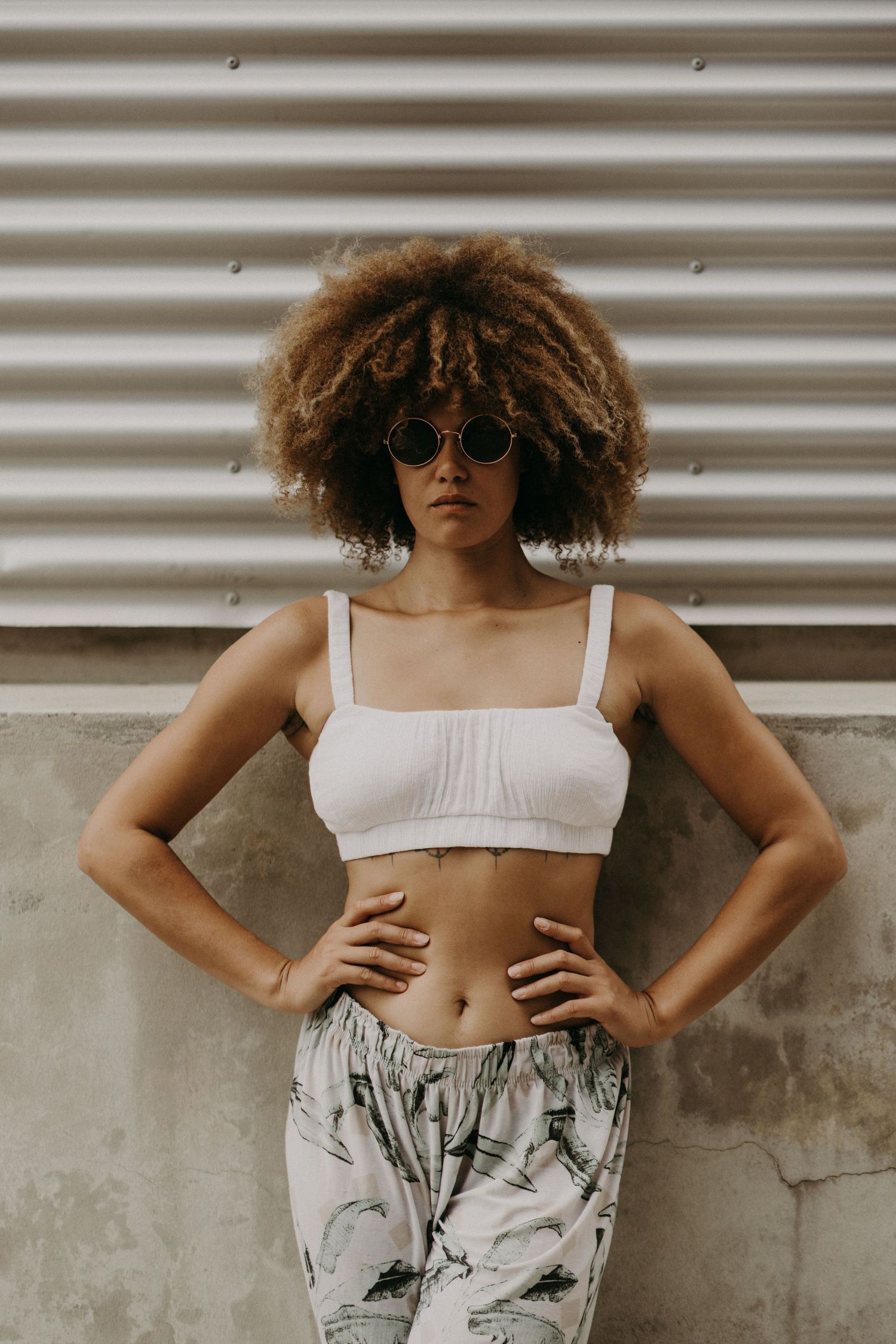 Fashion portrait of person in white crop top and patterned pants against industrial background.