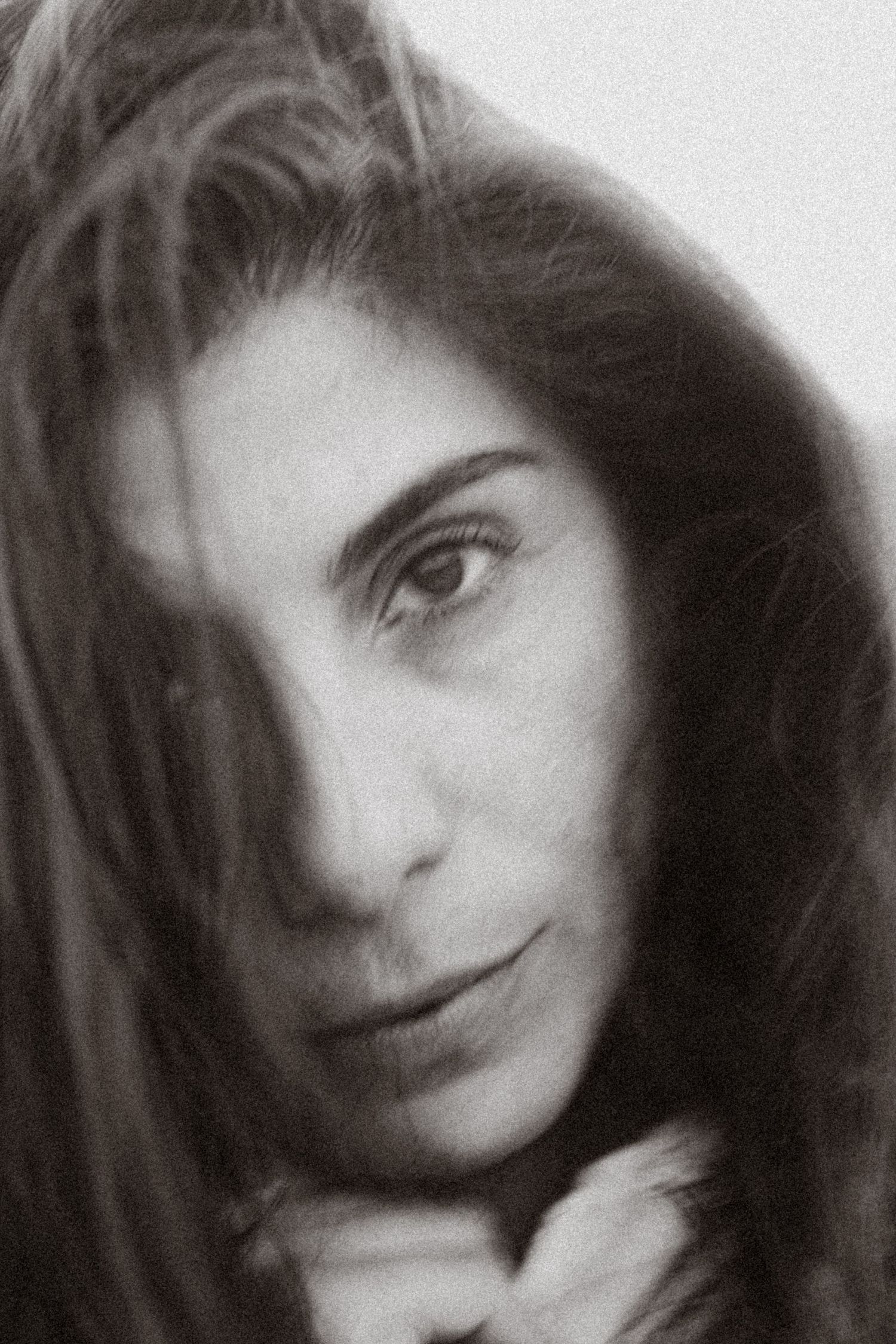Black and white close-up portrait of a woman with dark hair partially covering her face, gazing softly at the camera.