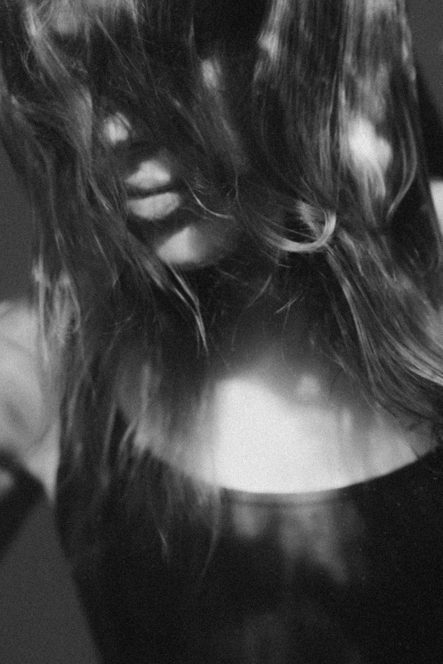 Black and white artistic portrait showing a side profile view of long flowing hair against a dark background.