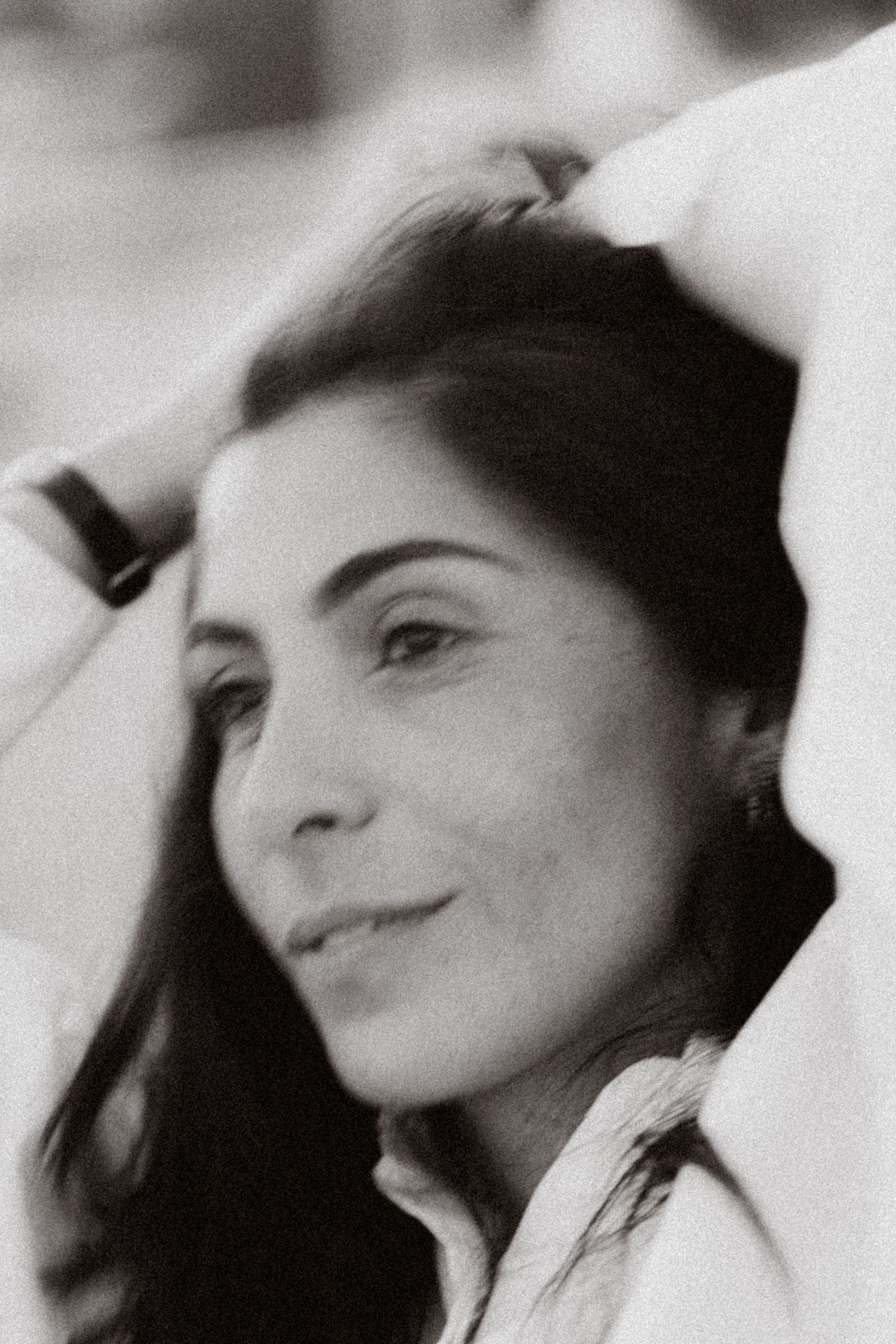 Black and white portrait of a young woman with dark hair, hands raised behind her head, smiling softly.